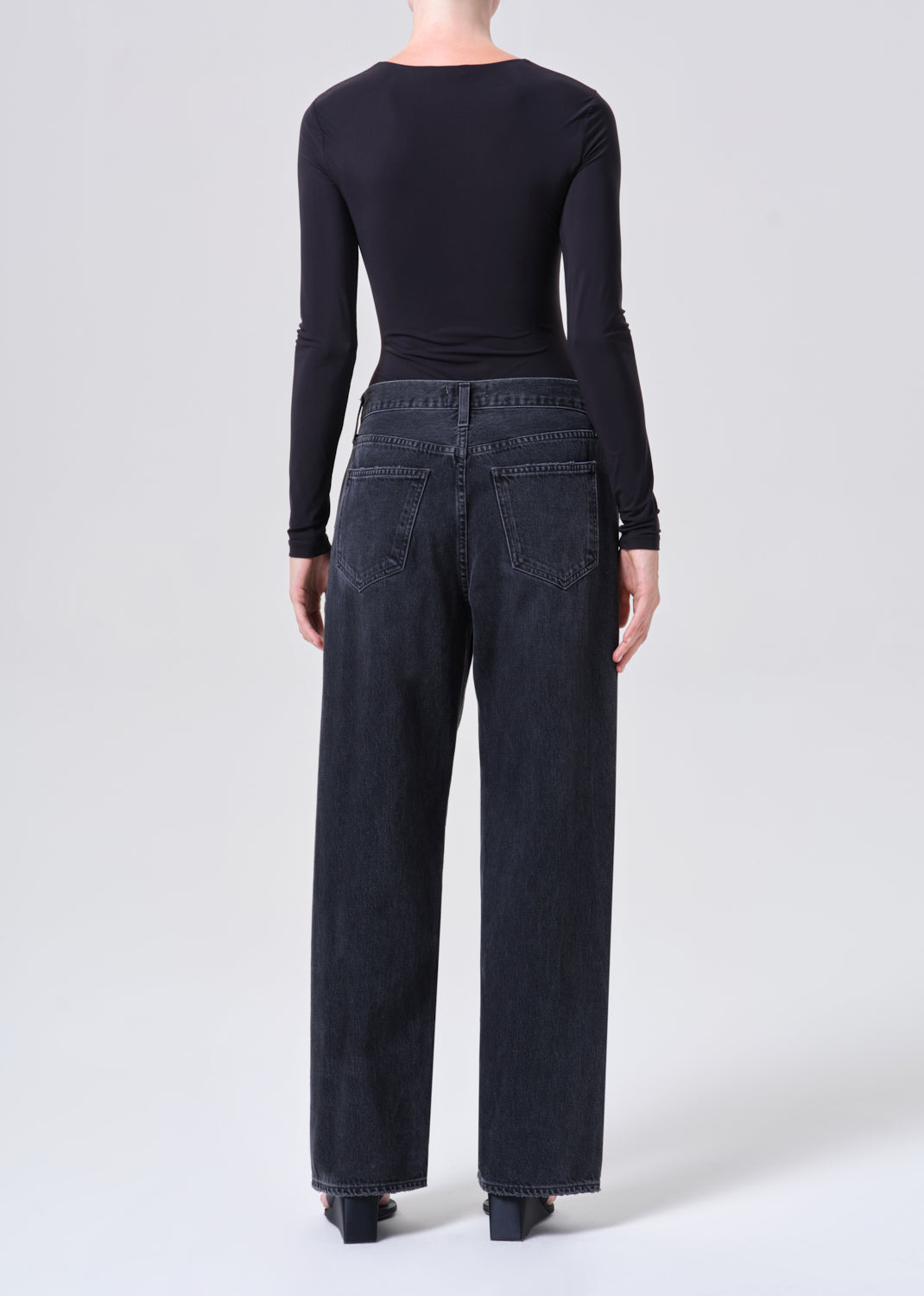 Person wearing black long-sleeve top and dark jeans on a white background