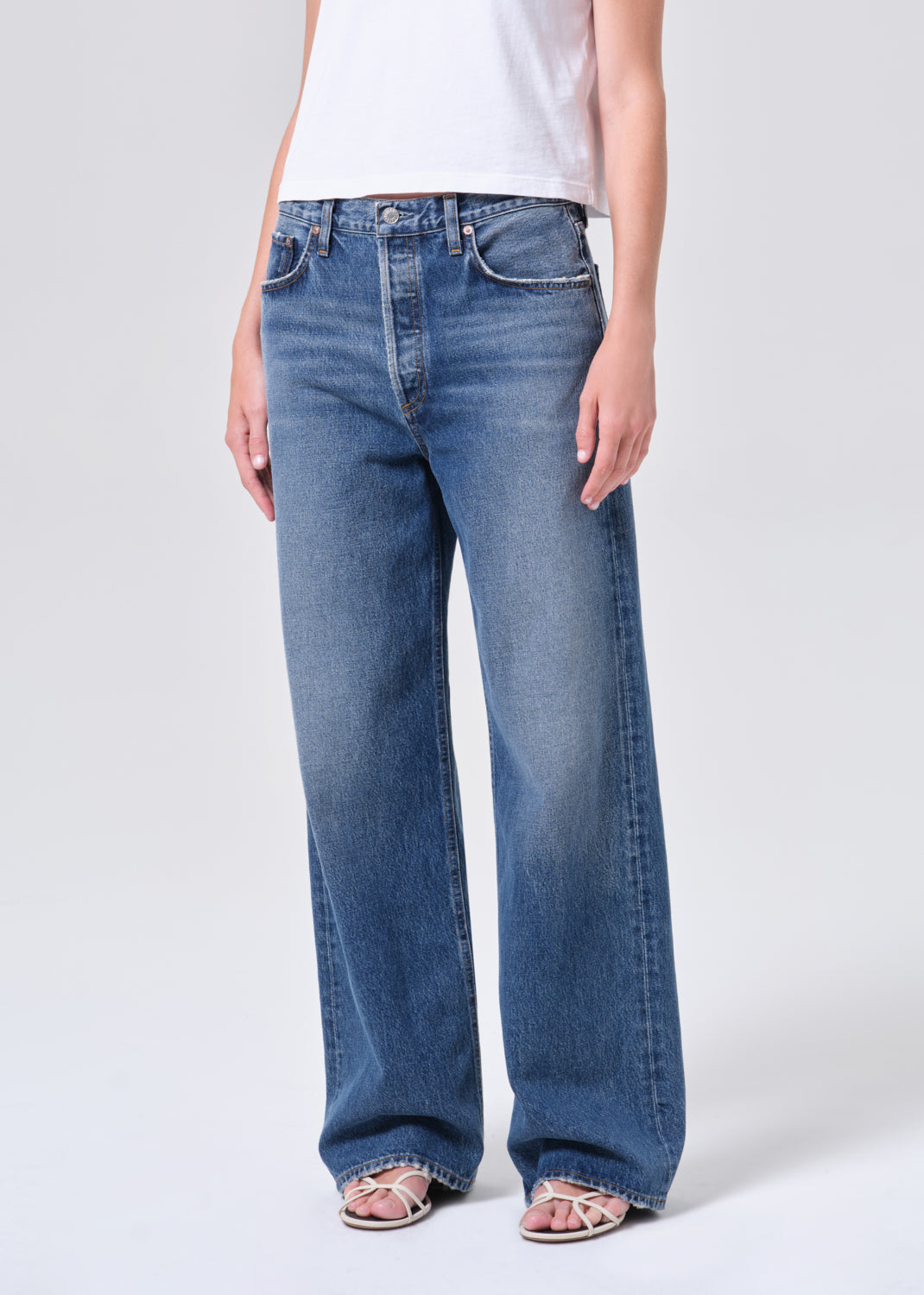 Person wearing blue jeans and a white shirt on a plain background