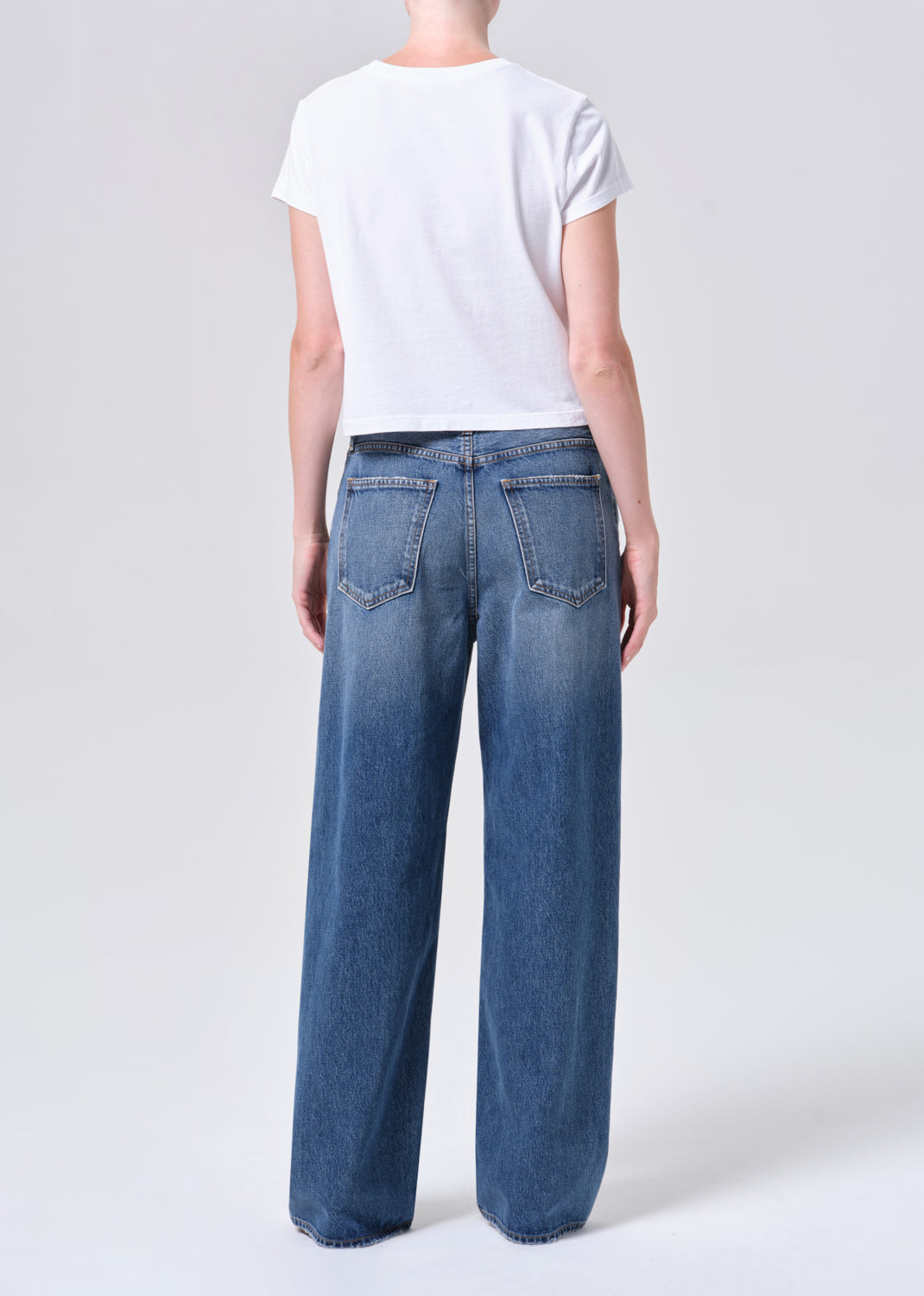 Person wearing blue jeans and a white t-shirt on a plain background