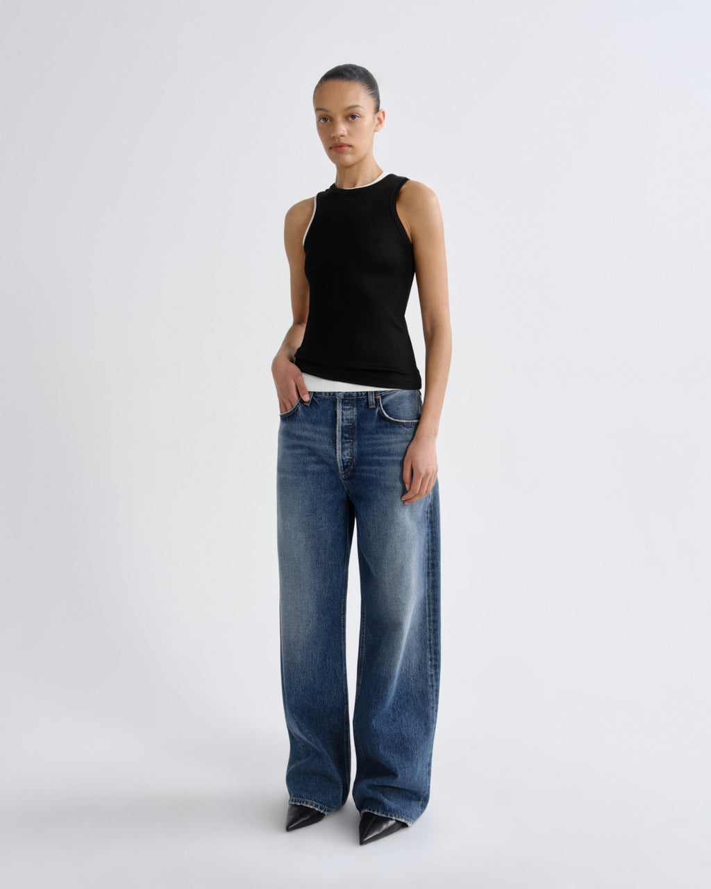 Person wearing a black sleeveless top and blue jeans on a white background