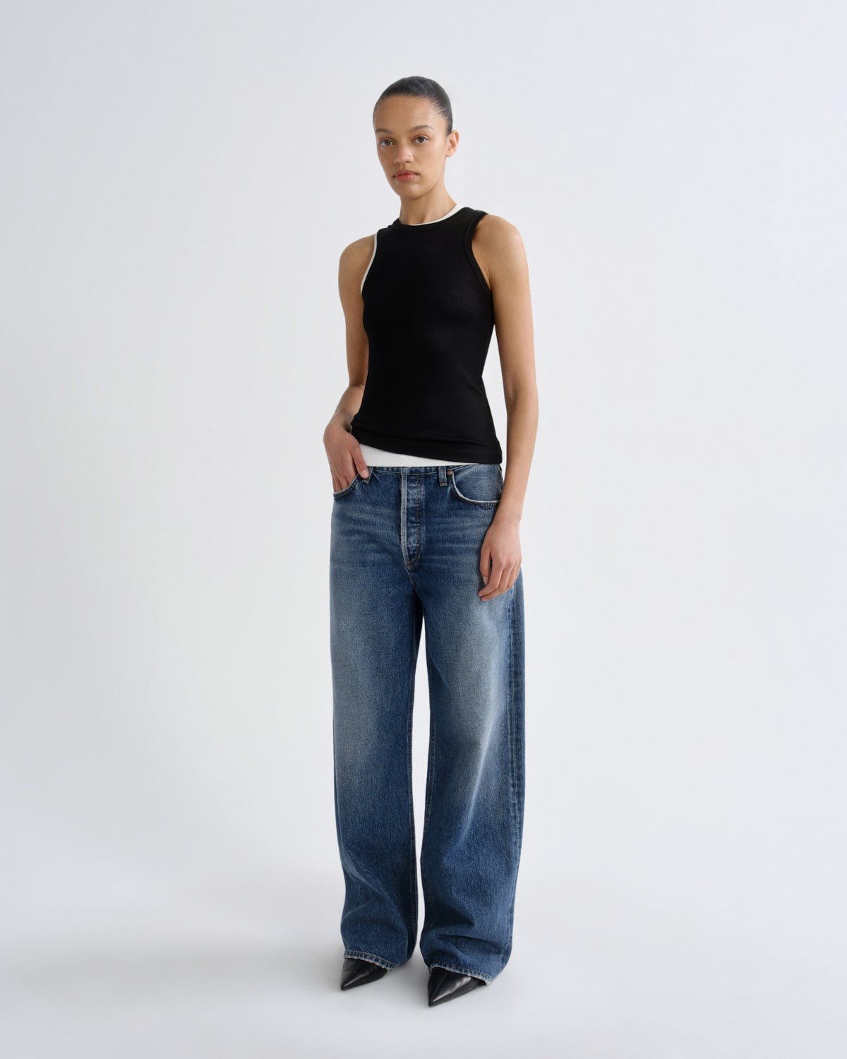 Person wearing a black sleeveless top and blue jeans on a white background