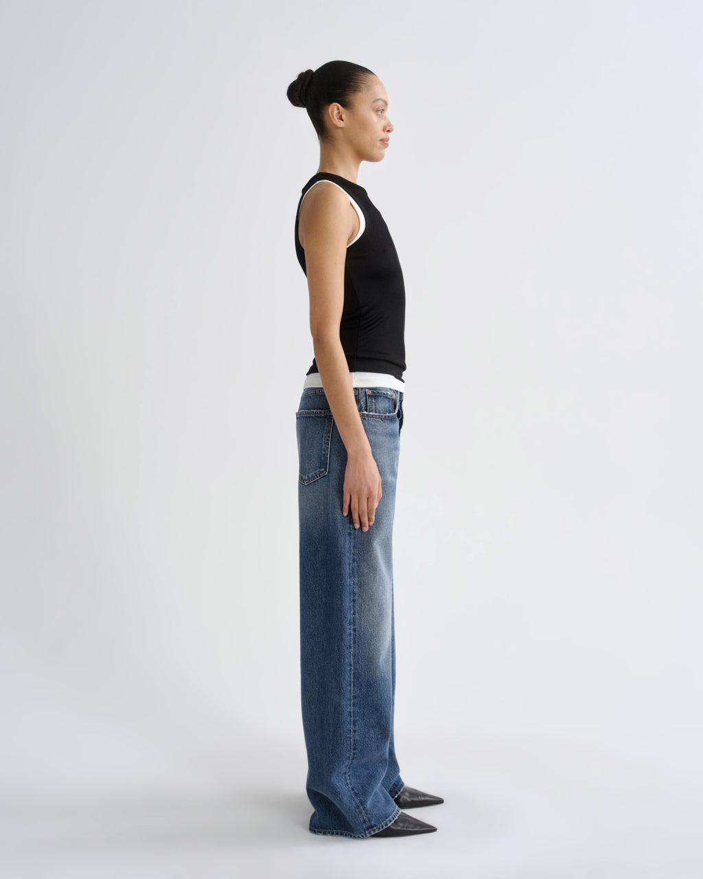 Person wearing blue jeans and a black top on a white background