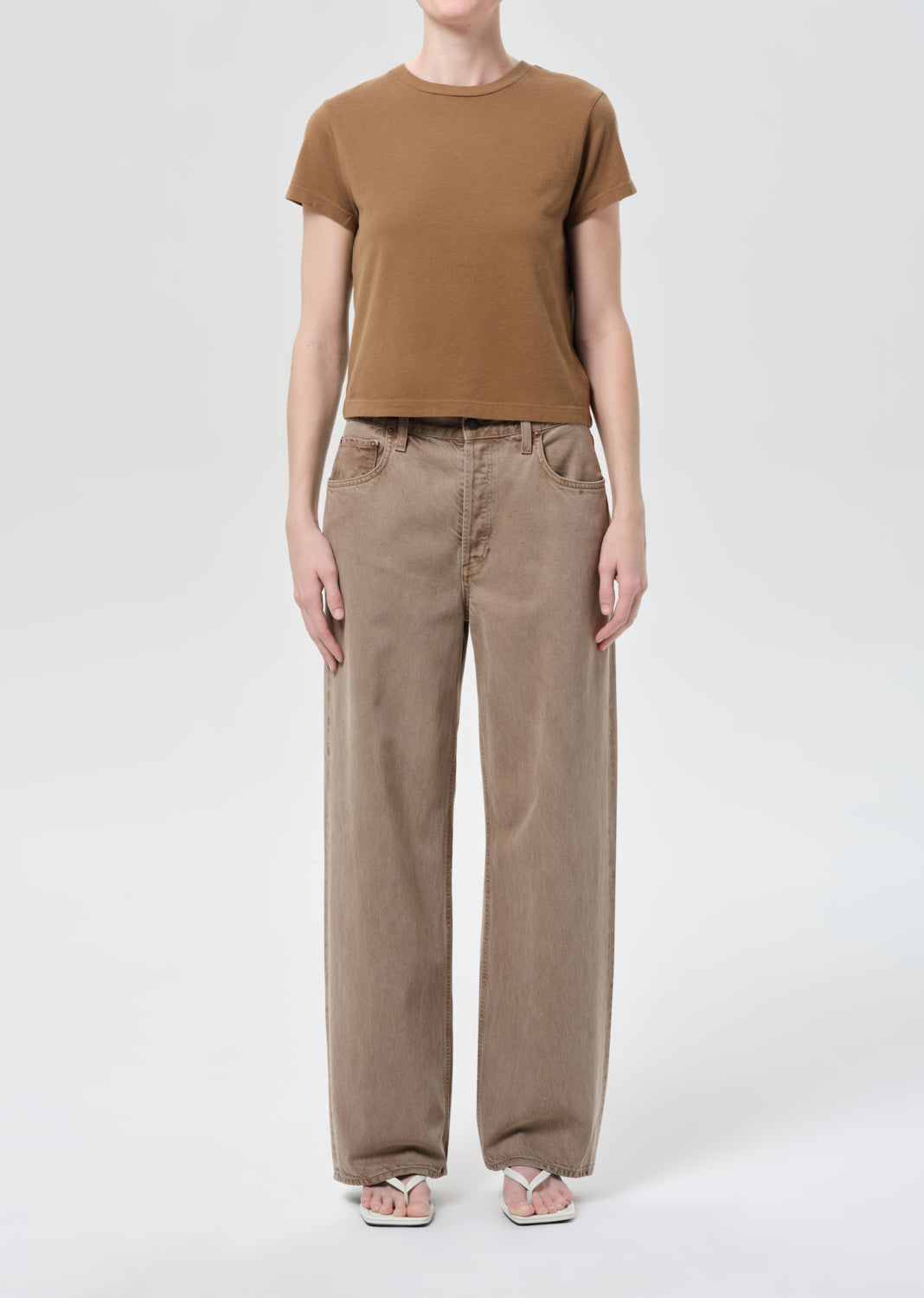 Person wearing a brown t-shirt and beige pants on a white background