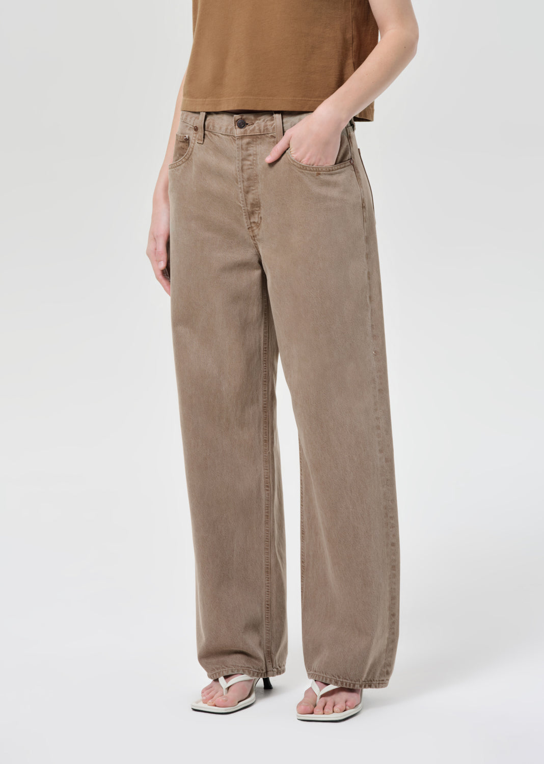 Person wearing beige pants and a brown top on a white background
