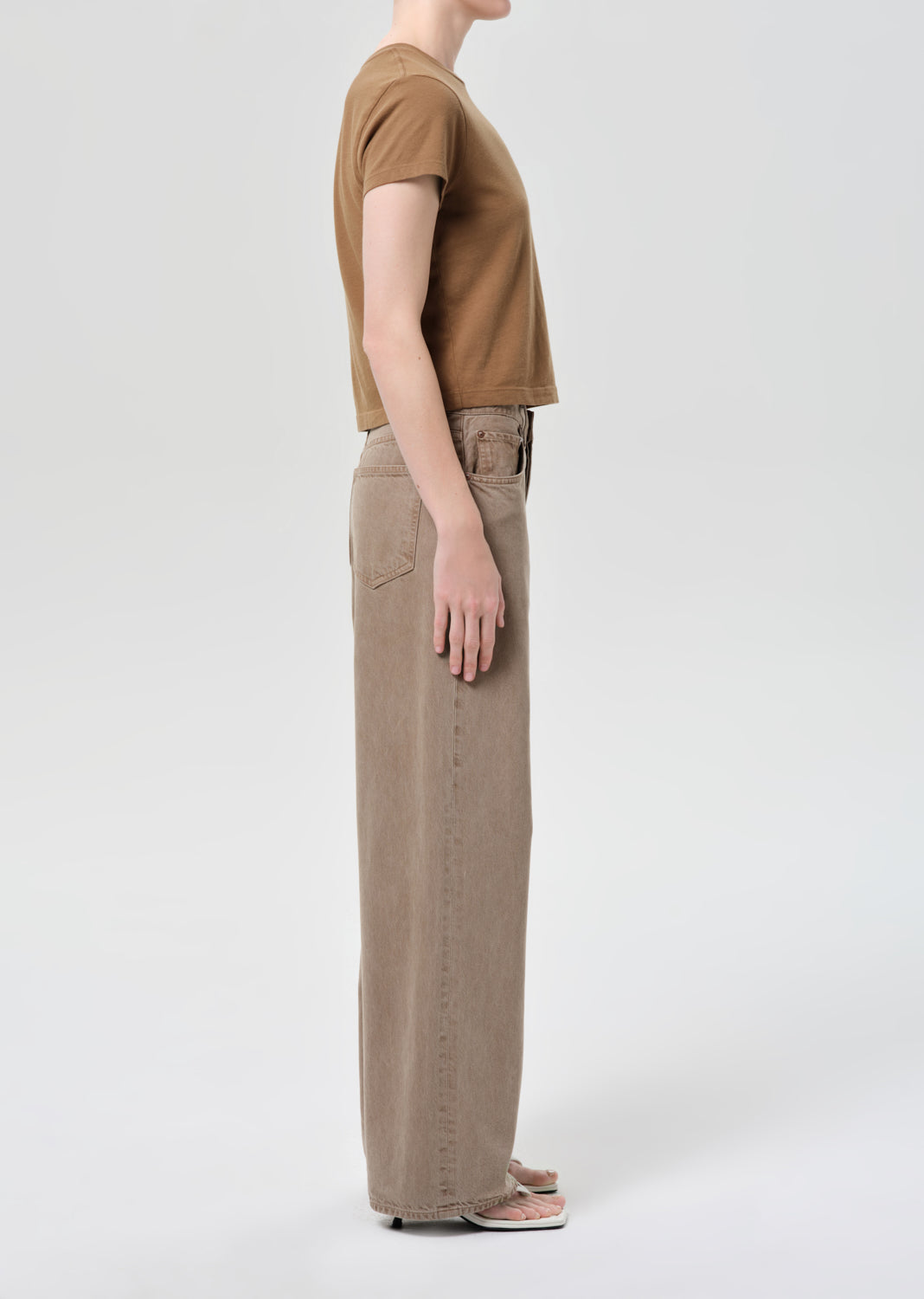 Person wearing a brown t-shirt and beige pants on a white background