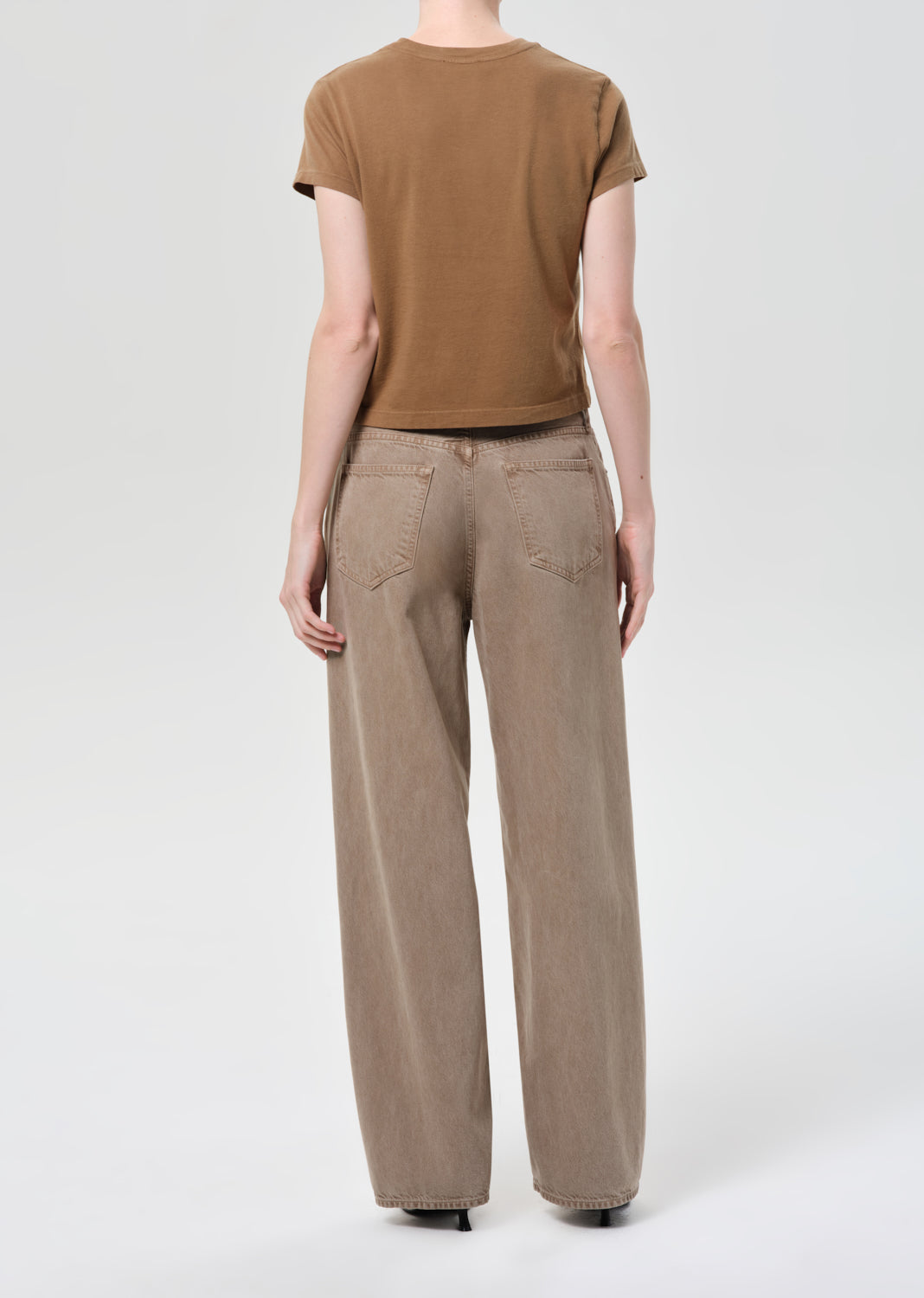 Person wearing a brown t-shirt and beige pants on a white background