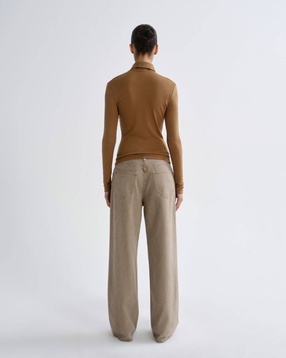 Person wearing a brown long-sleeve top and beige pants on a white background