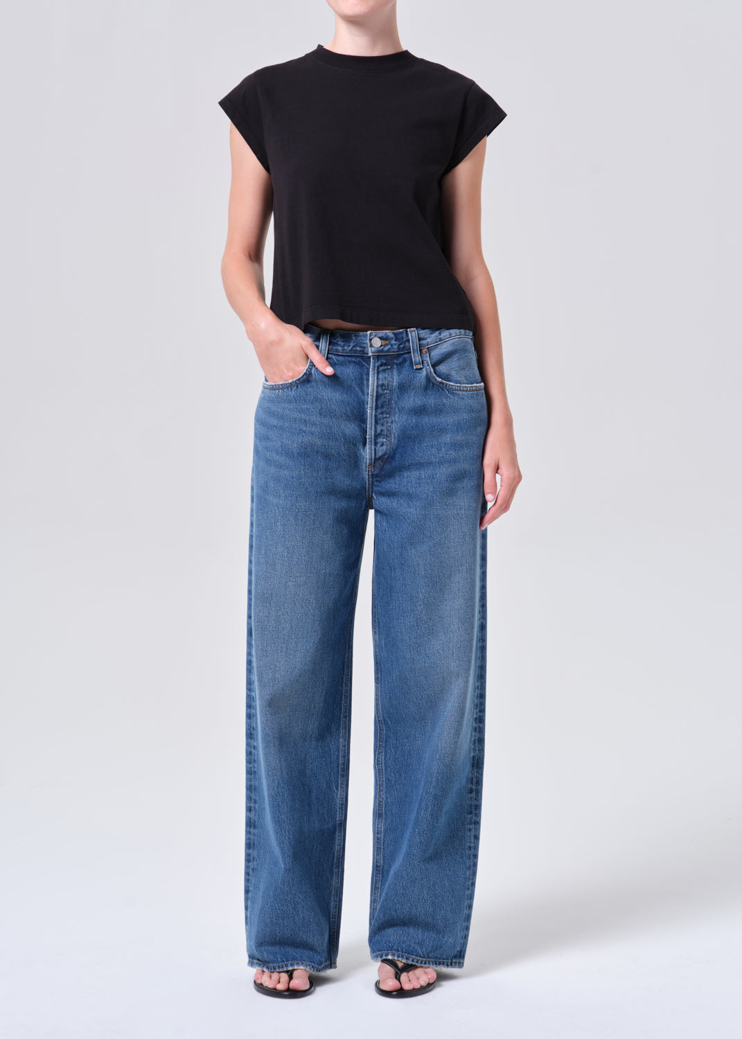 Person wearing a black top and blue jeans on a white background