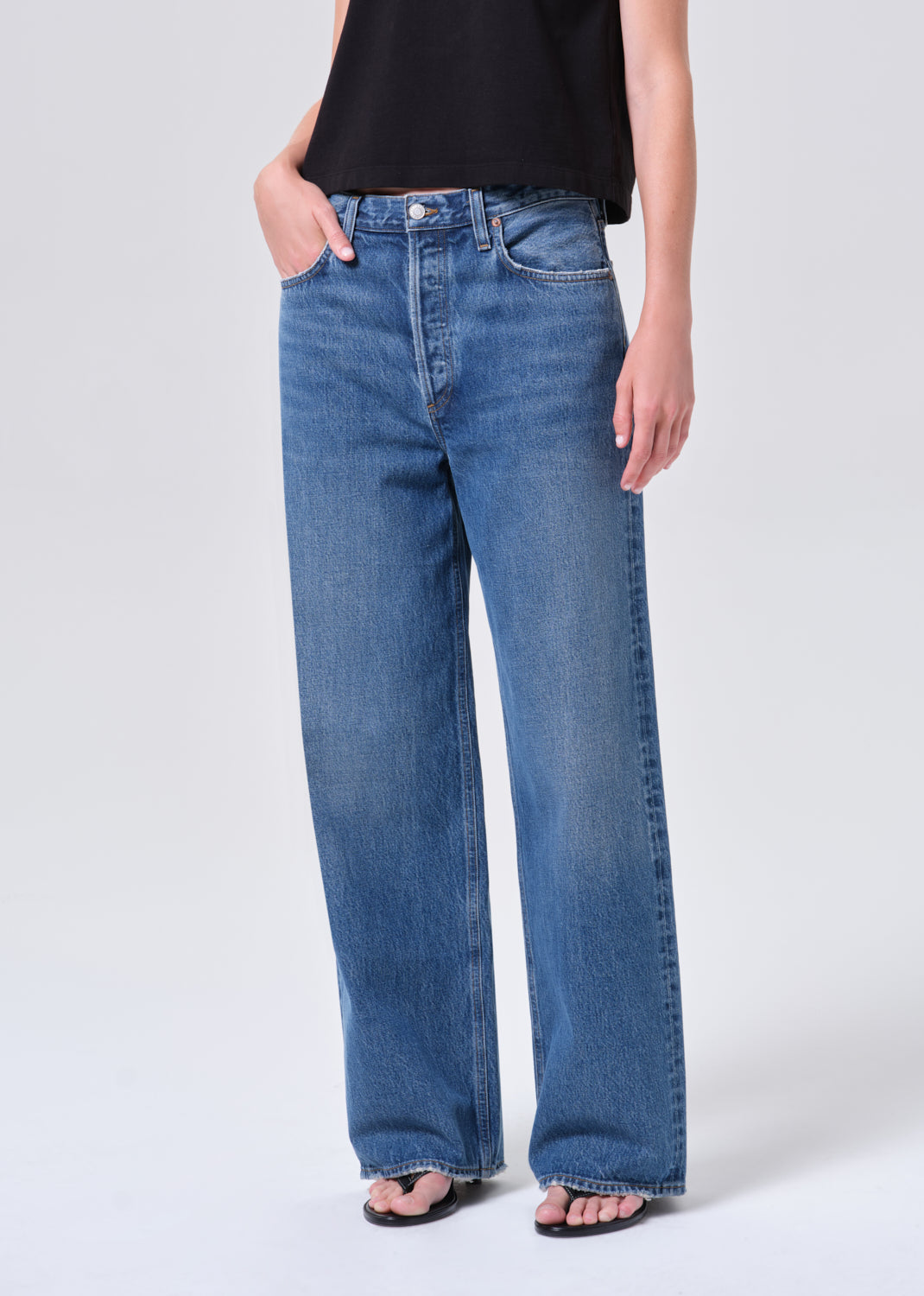 Person wearing blue jeans and a black top on a white background