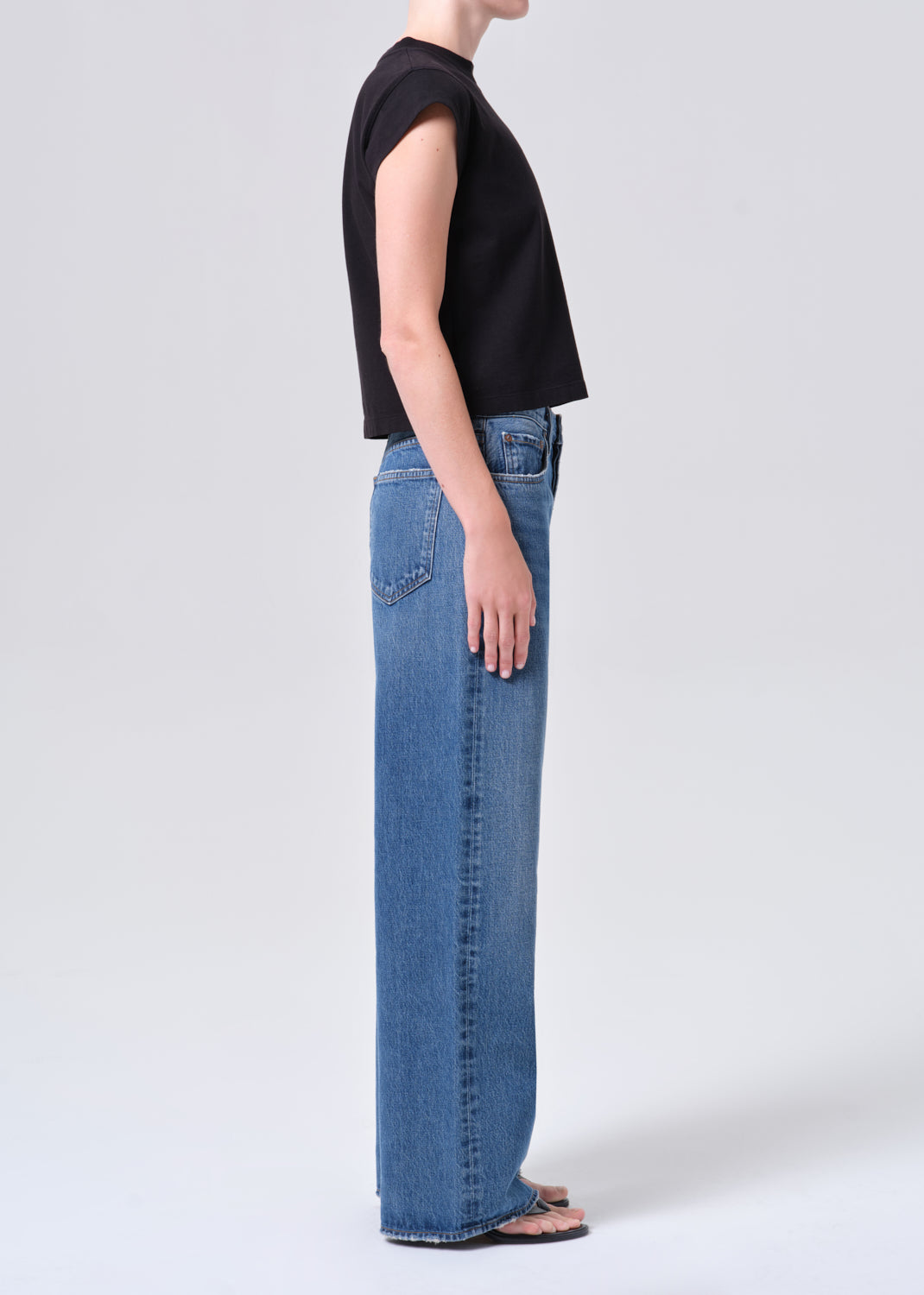 Person wearing blue jeans and a black top on a white background