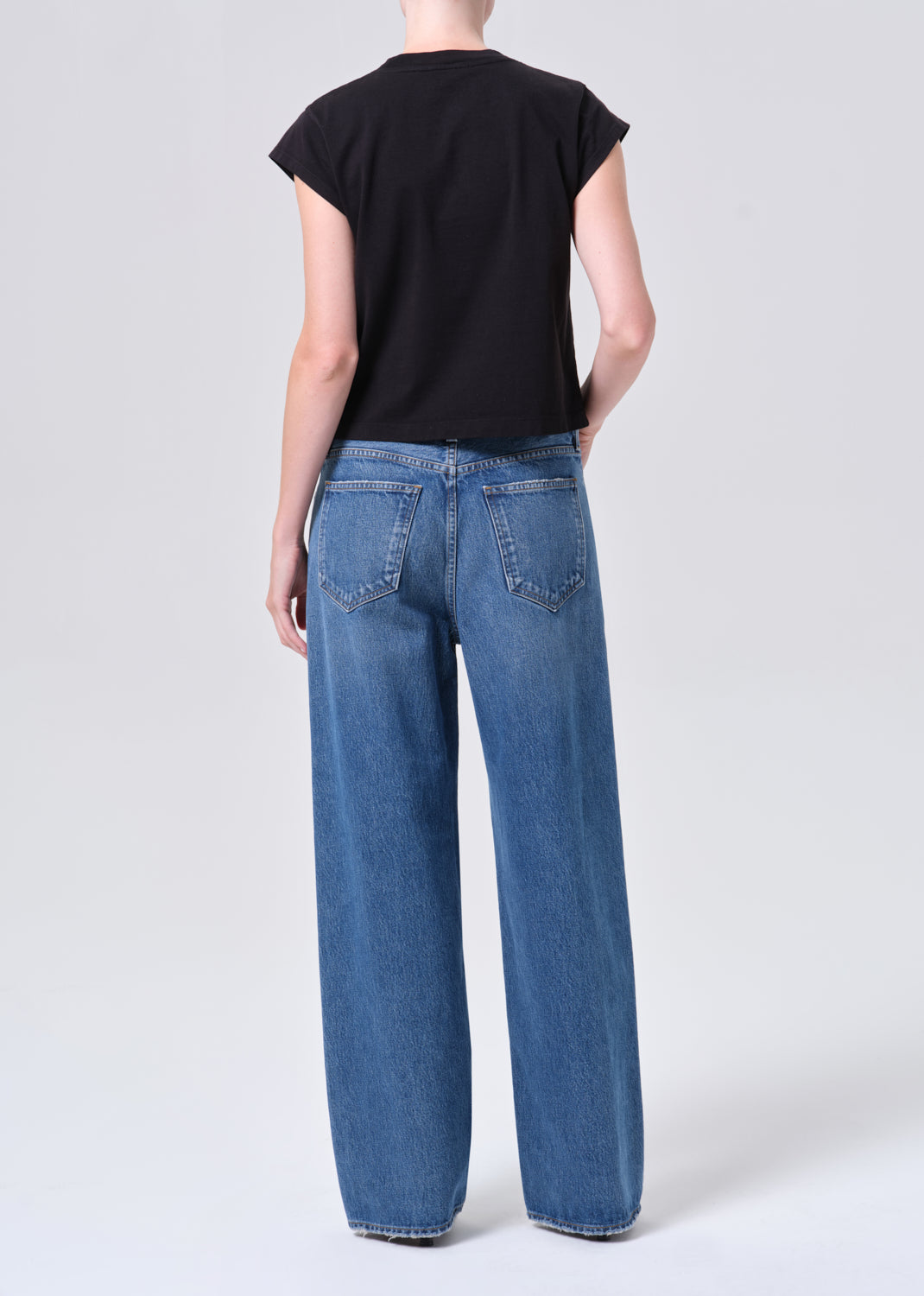 Person wearing blue jeans and a black top on a white background
