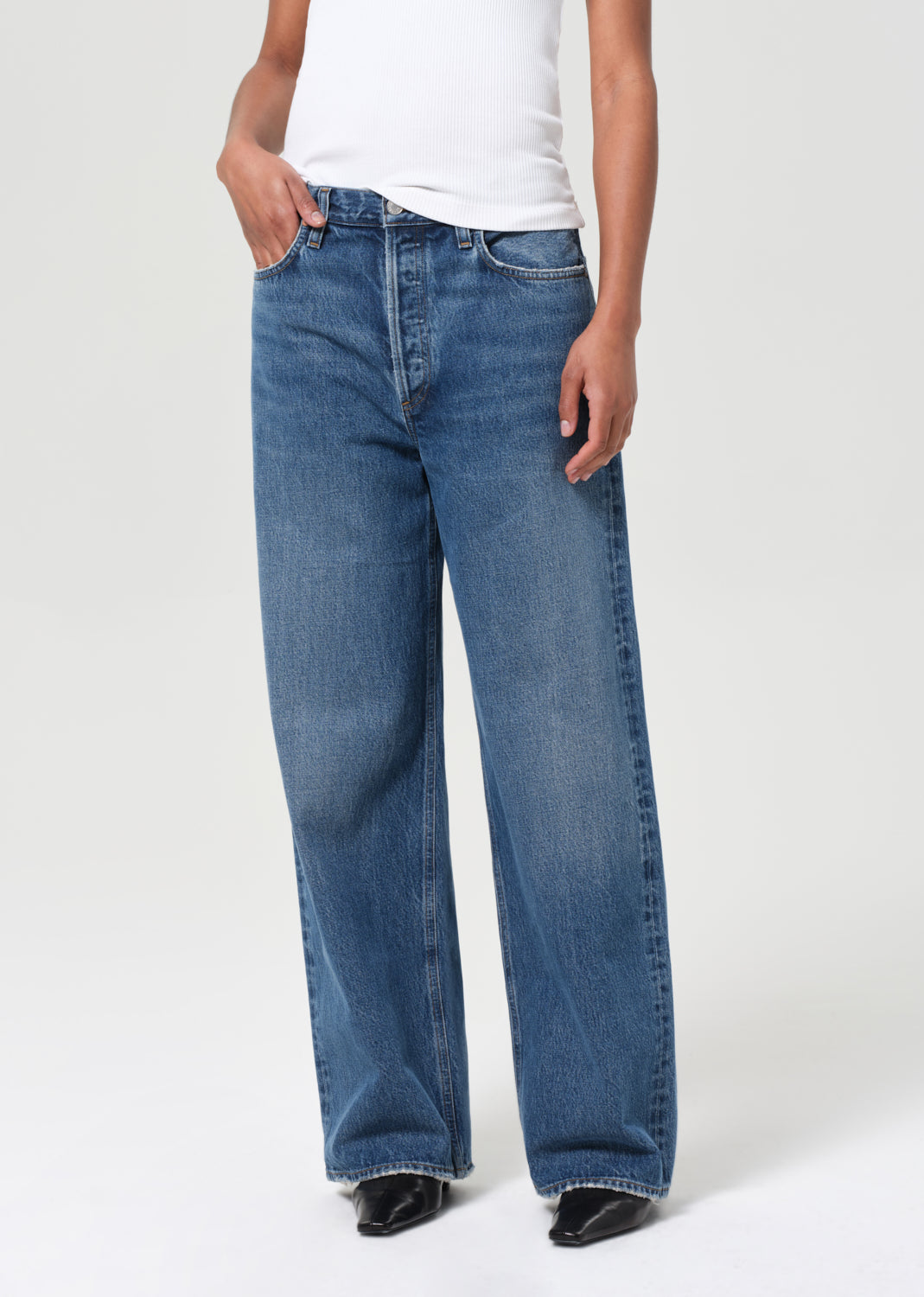 Person wearing blue jeans and a white shirt on a plain background
