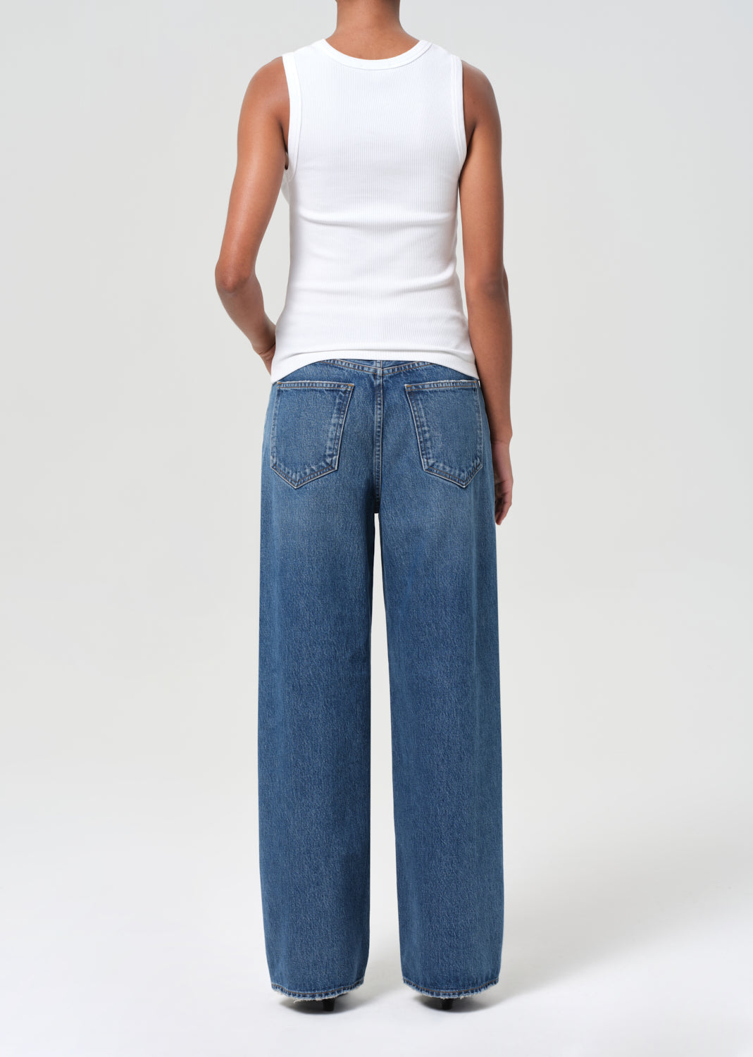 Person wearing a white sleeveless top and blue jeans on a plain background