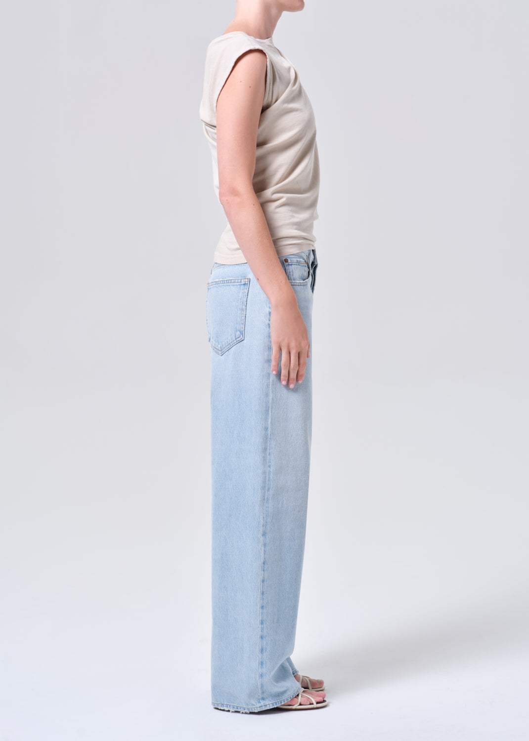 Person wearing a beige sleeveless top and light blue jeans on a white background