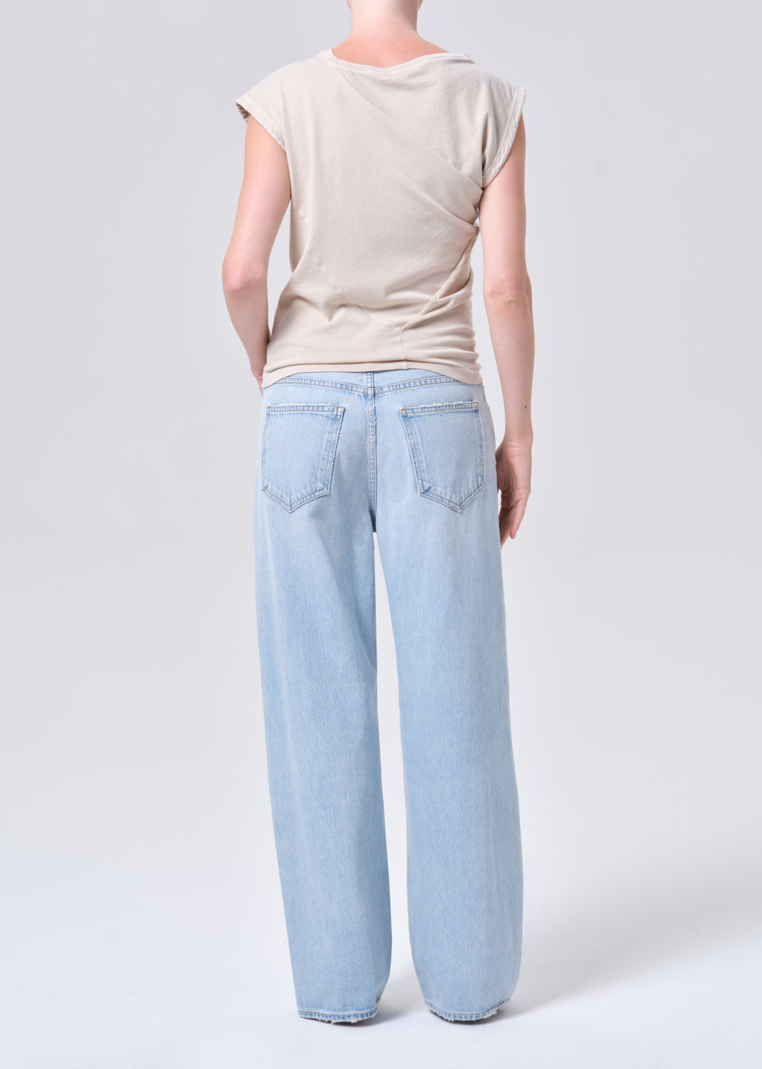 Person wearing light blue jeans and a beige top on a white background