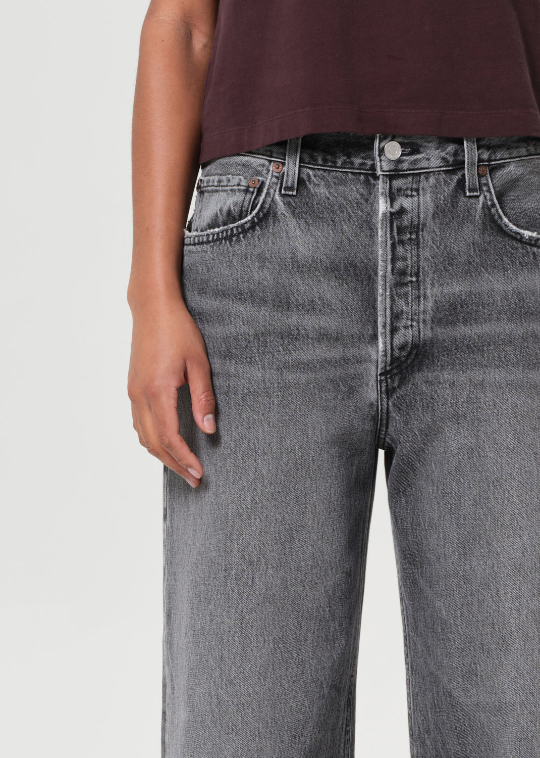 Person wearing gray jeans and a maroon top on a light gray background