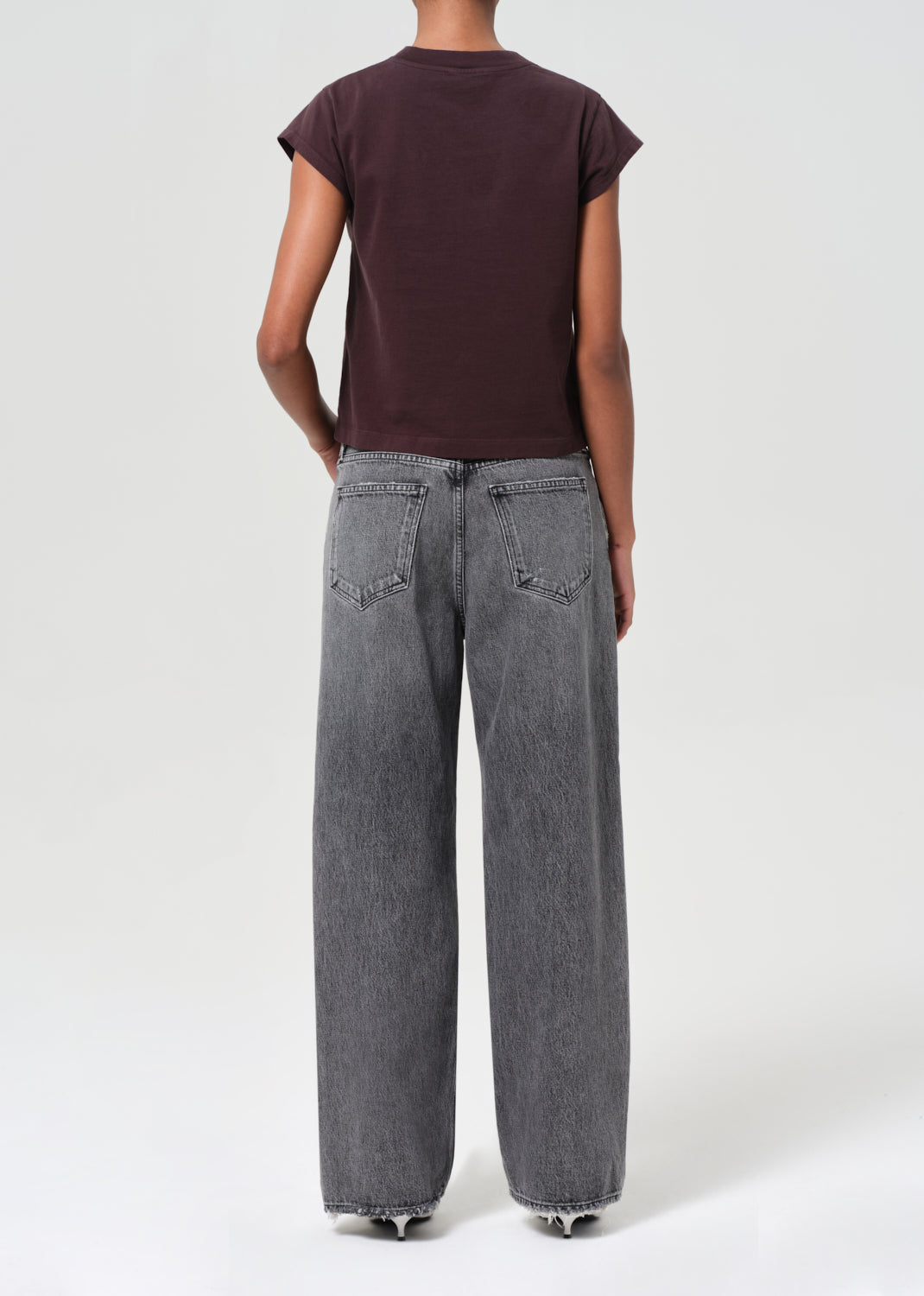 Person wearing a dark brown t-shirt and gray jeans on a white background