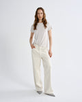 Woman wearing a white t-shirt and cream-colored pants on a plain background