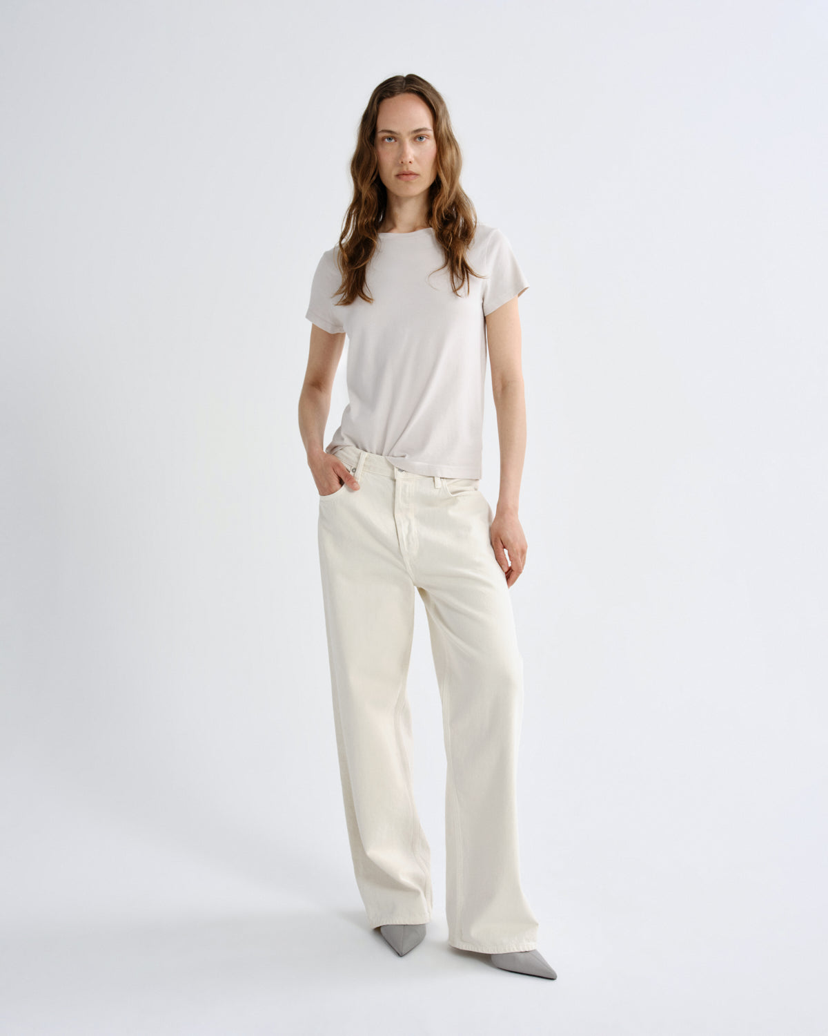Woman wearing a white t-shirt and cream-colored pants on a plain background