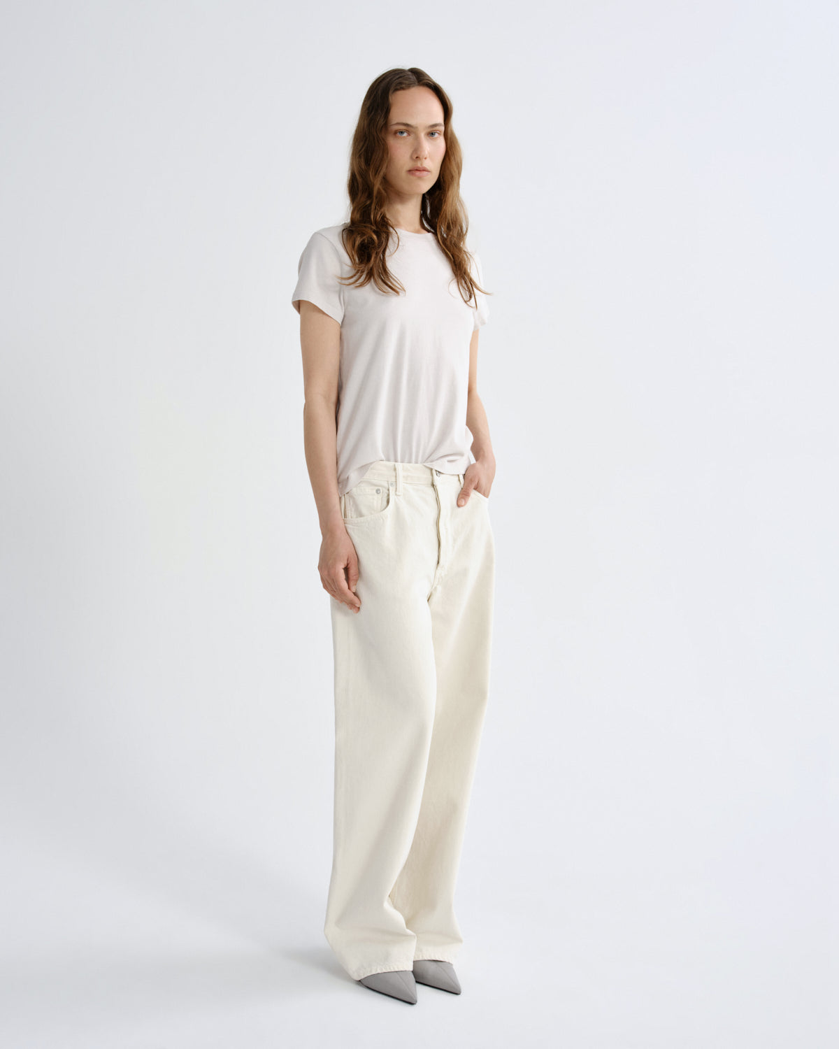 Person wearing a white t-shirt and cream-colored pants on a light gray background