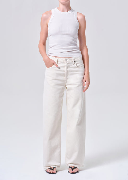 Person wearing a white sleeveless top and light-colored pants on a plain background