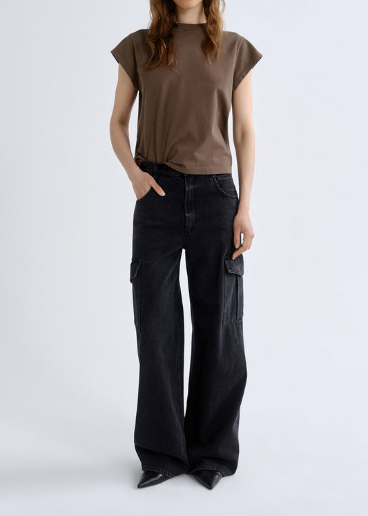Person wearing a brown cap sleeve tee with black wide leg jeans on a grey background.