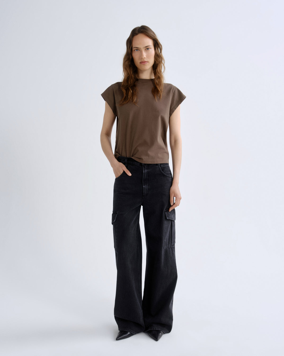 Woman wearing a brown top and black pants on a white background