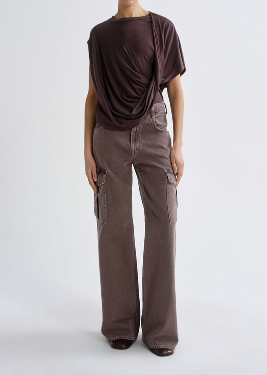 A model wearing a dark brown draped short-sleeve top and wide-leg cargo pants in a muted taupe-brown color, photographed against a grey background.