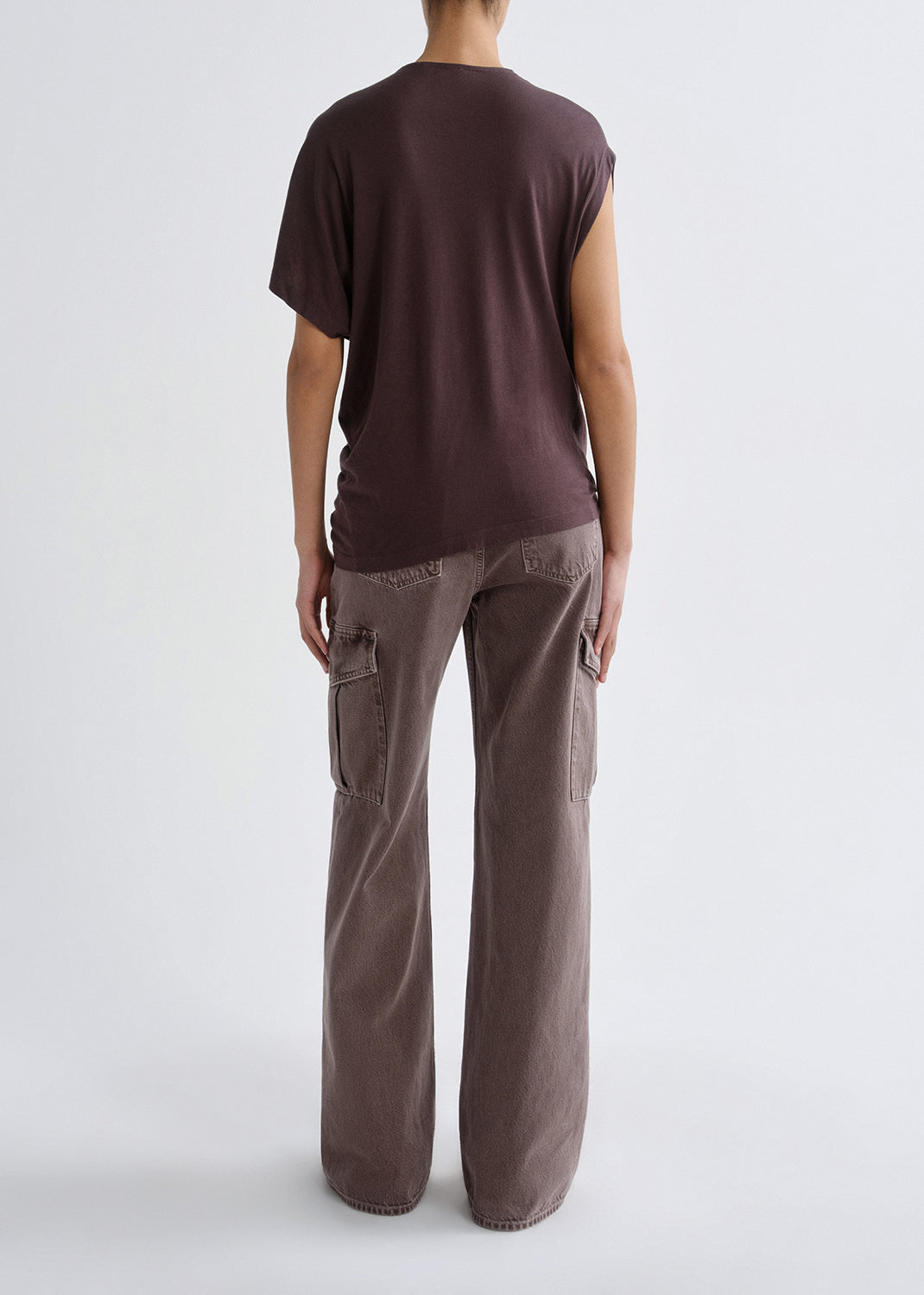 A model shown from the back wearing a dark brown short-sleeve t-shirt and wide-leg brown pants against a grey background.