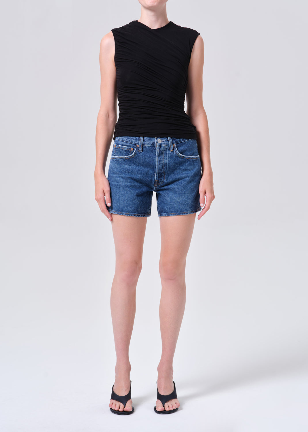 Person wearing a black sleeveless top and blue denim shorts on a white background