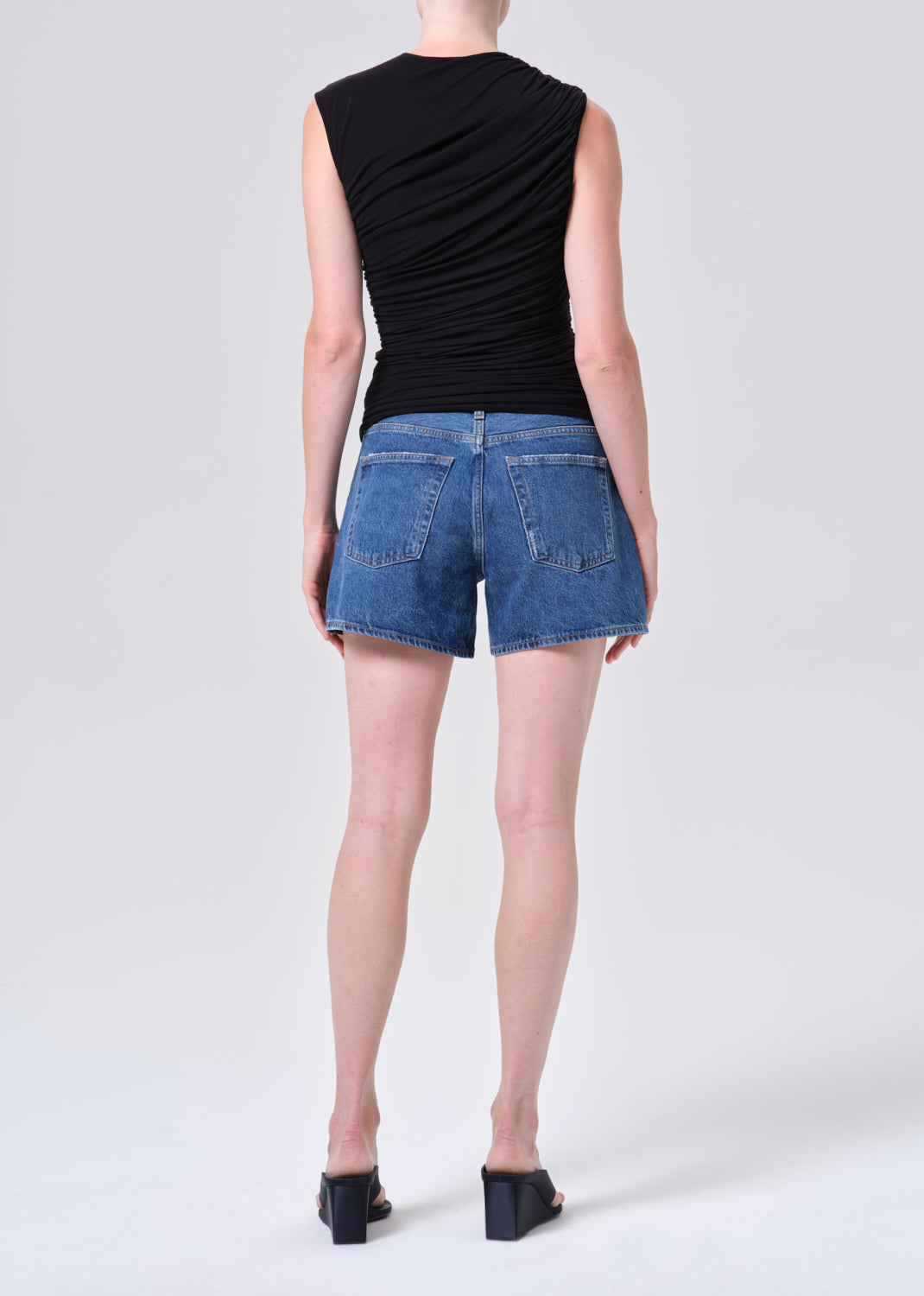 Person wearing a black sleeveless top and blue denim shorts on a white background