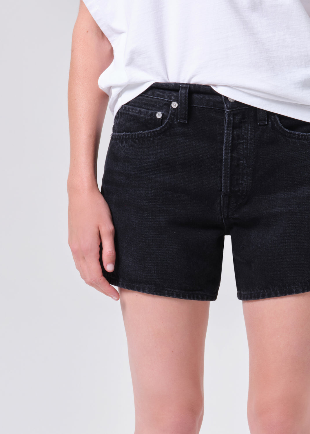 Person wearing black denim shorts on a plain background