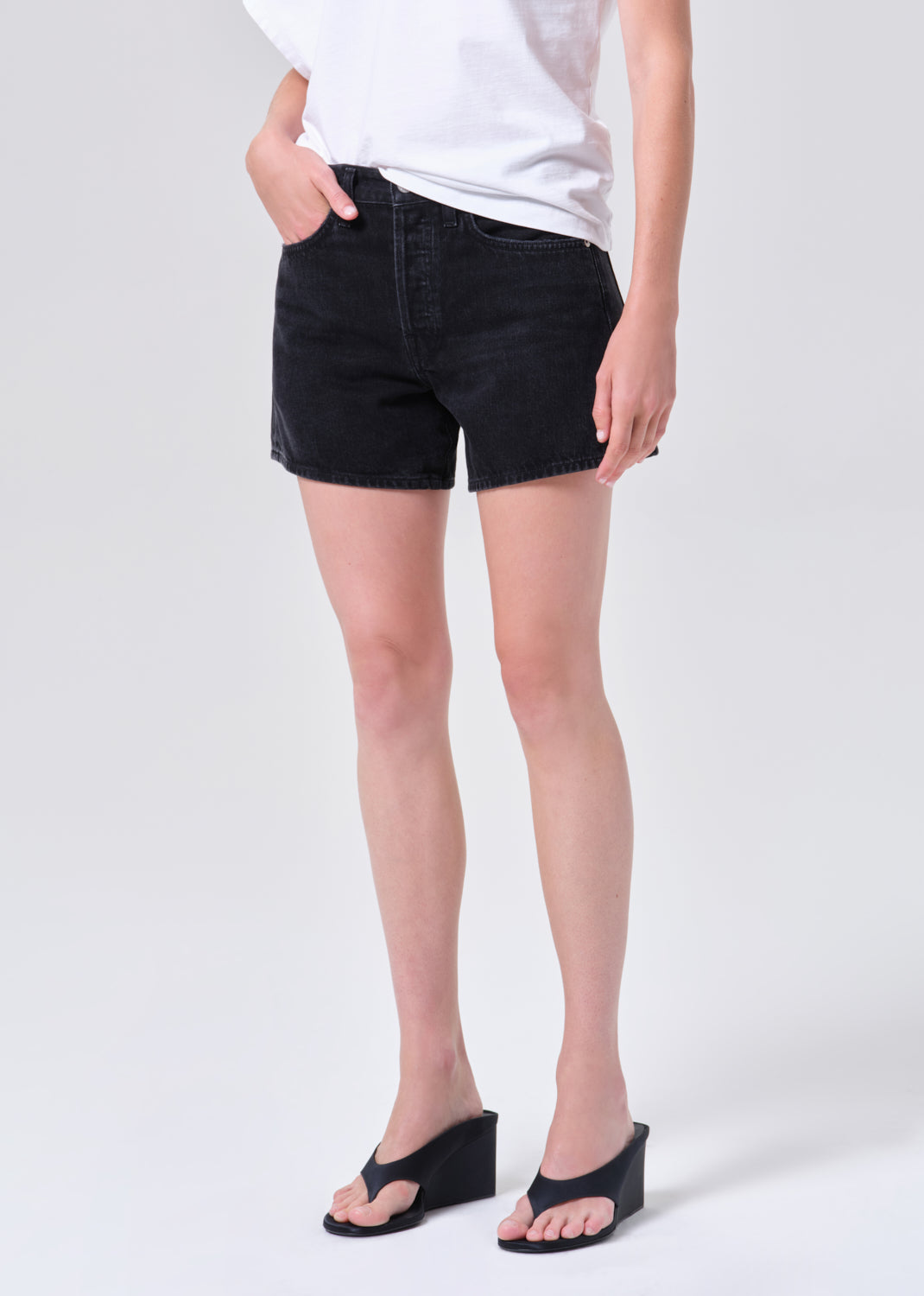Person wearing black denim shorts on a white background