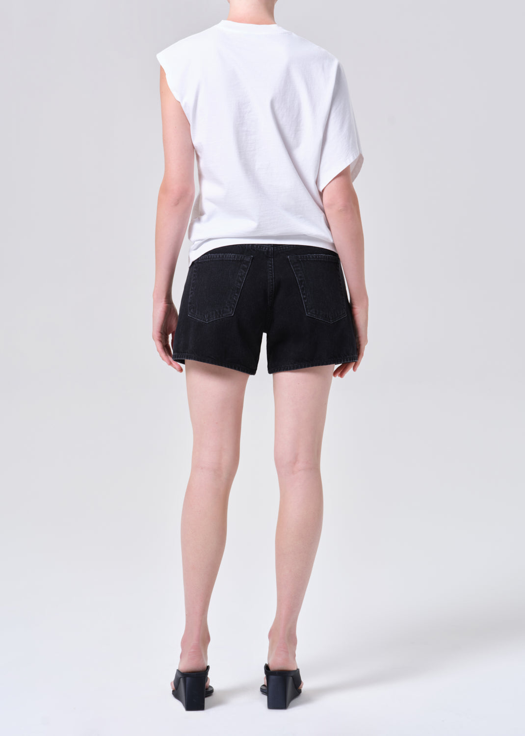 Person wearing a white sleeveless top and black shorts on a plain background