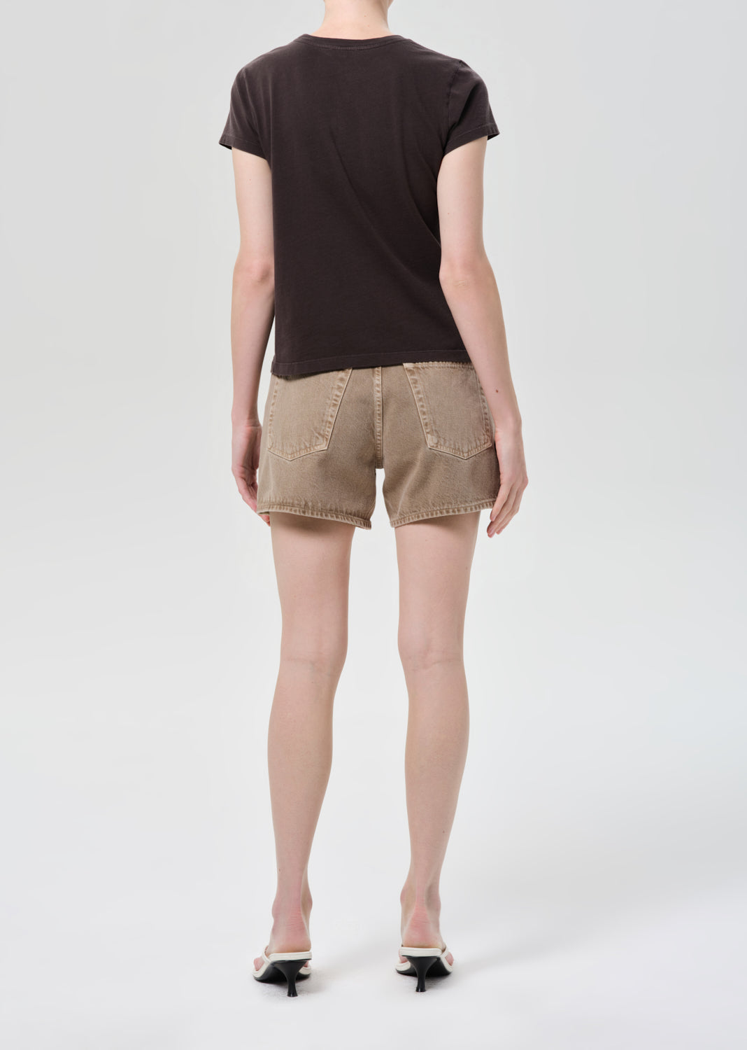 Person wearing a black t-shirt and beige shorts on a white background