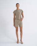 A model stands against a light gray studio background wearing a taupe short-sleeve crewneck t-shirt, matching beige denim shorts, and beige strappy high-heeled sandals.