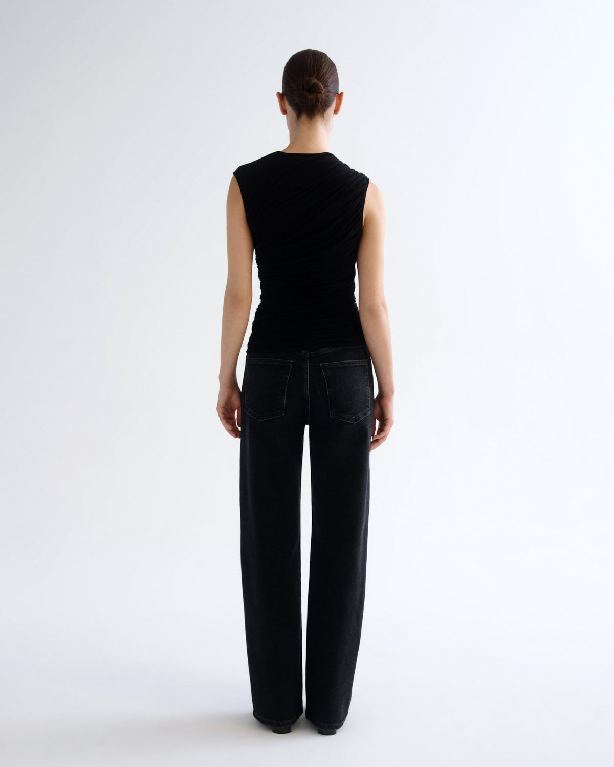 A model shown from the back wearing a black sleeveless top and black wide-leg jeans against a plain white studio background.