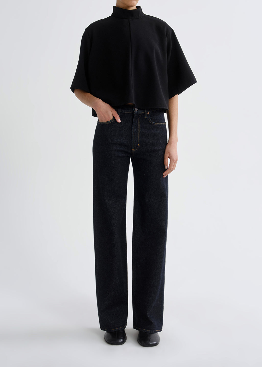 Person wearing a black turtleneck and dark jeans on a grey background