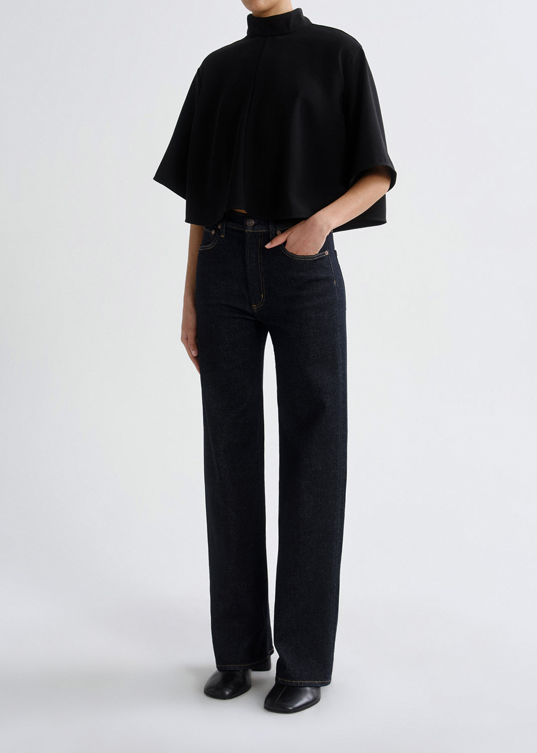 Person wearing a black turtleneck and black jeans on a grey background