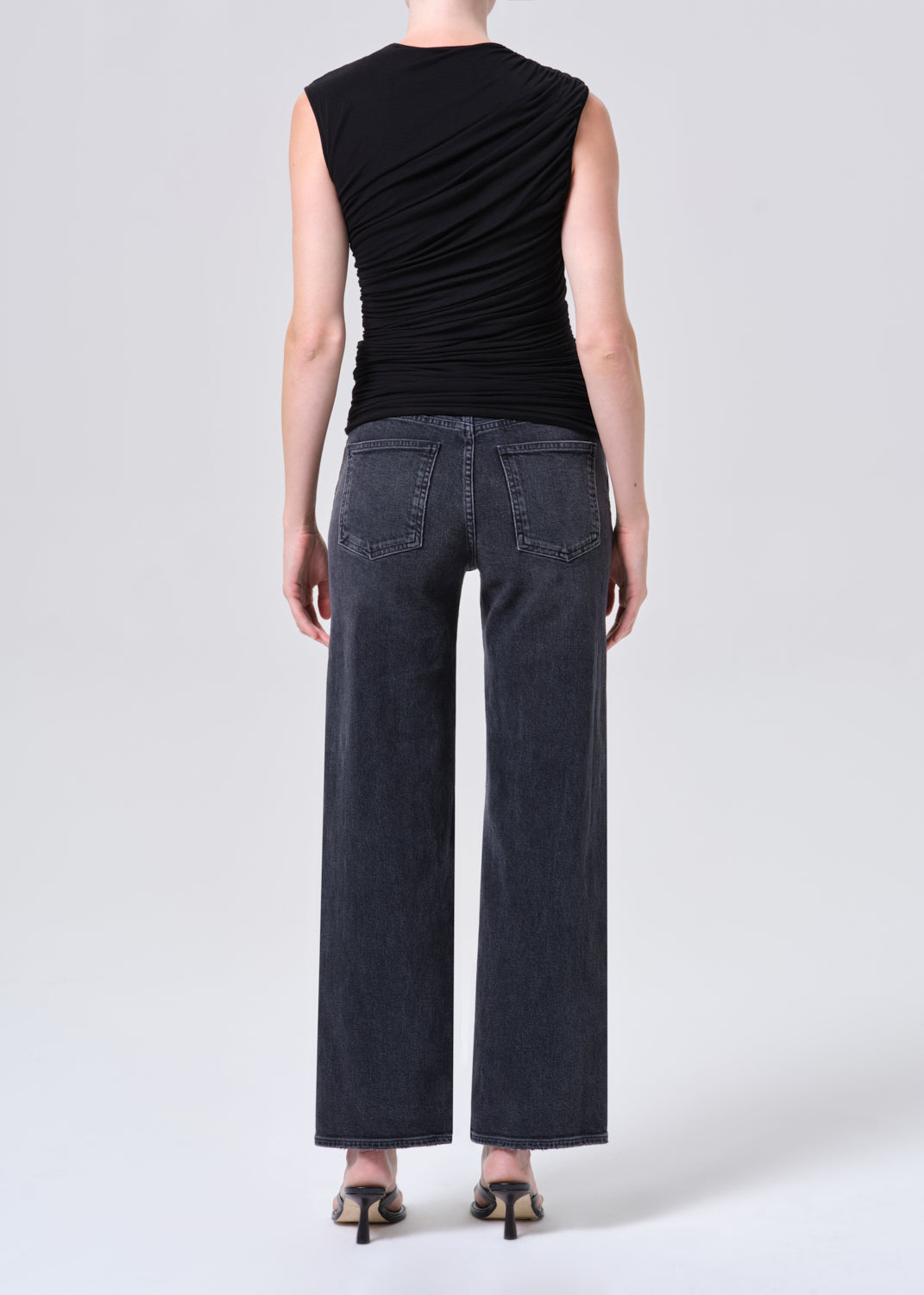 Person wearing a black sleeveless top and dark jeans on a white background