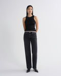 A model stands against a light gray studio background wearing a black sleeveless ribbed top, dark gray wide-leg jeans, and black pointed shoes.