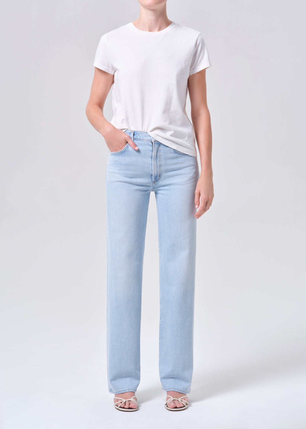 Person wearing a white t-shirt and light blue jeans on a plain background