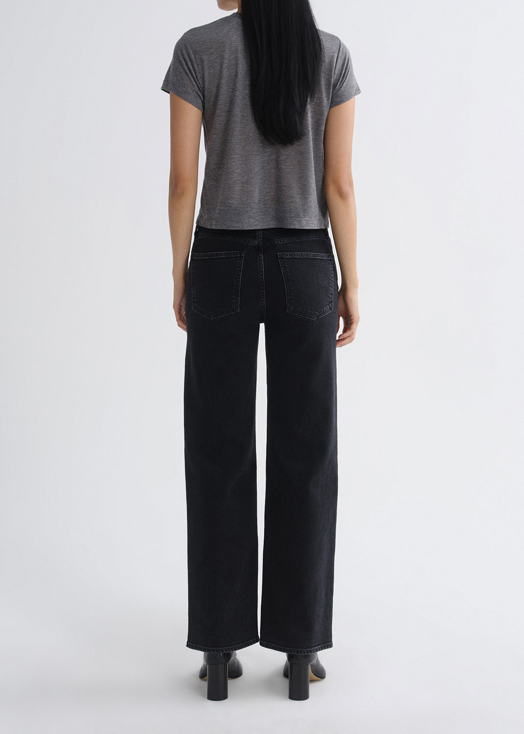 Person wearing black wide-leg jeans and a gray t-shirt on a grey background