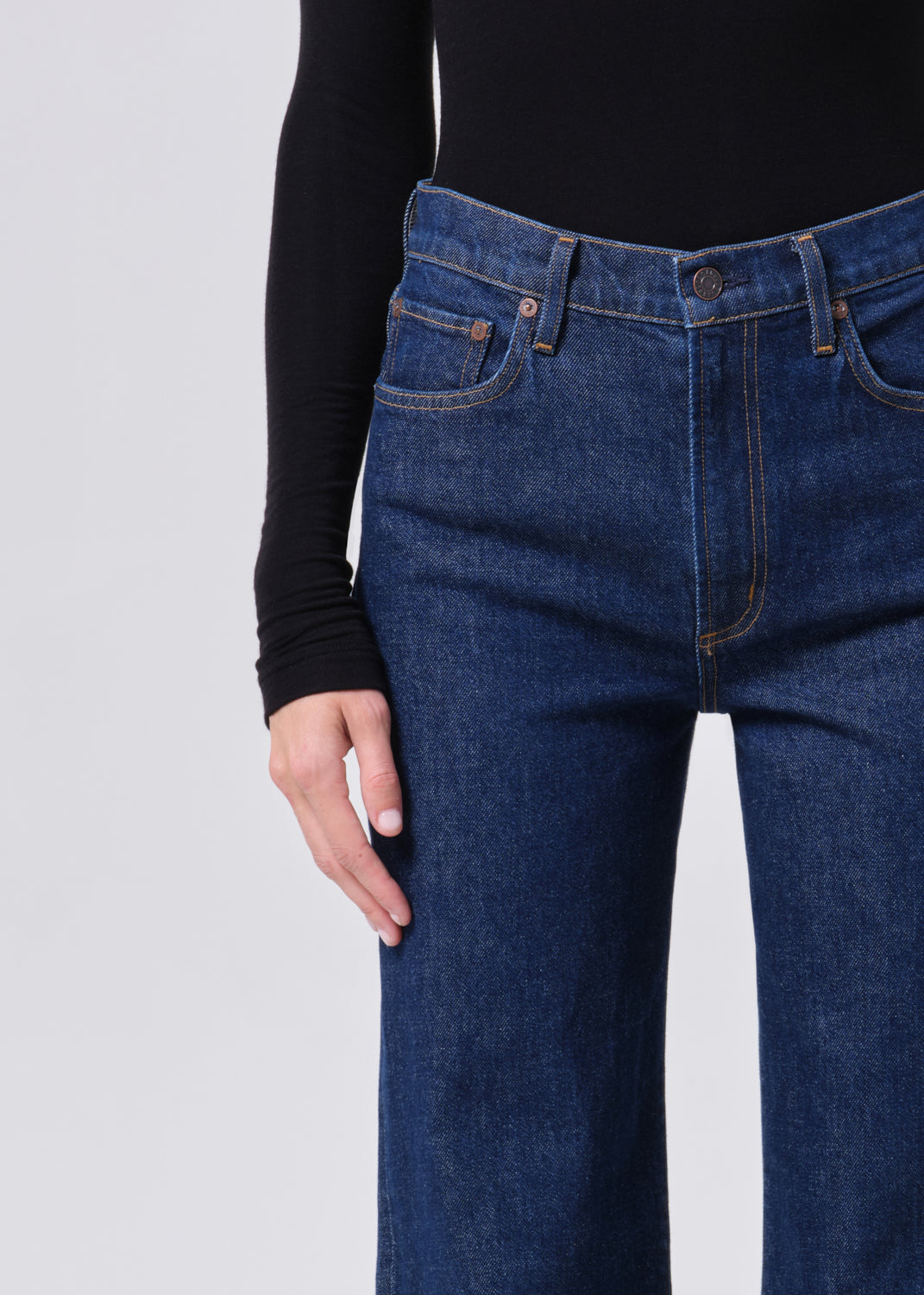 Person wearing blue jeans and a black long-sleeve shirt on a light gray background