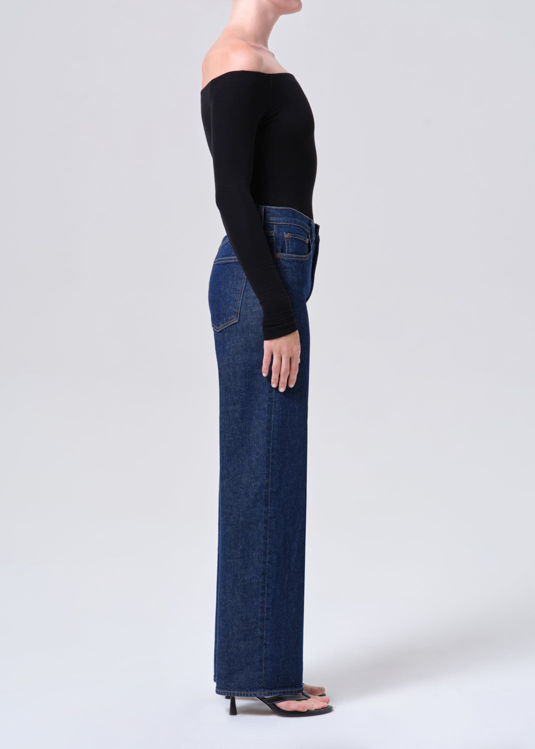 Person wearing a black long-sleeve top and blue jeans on a white background