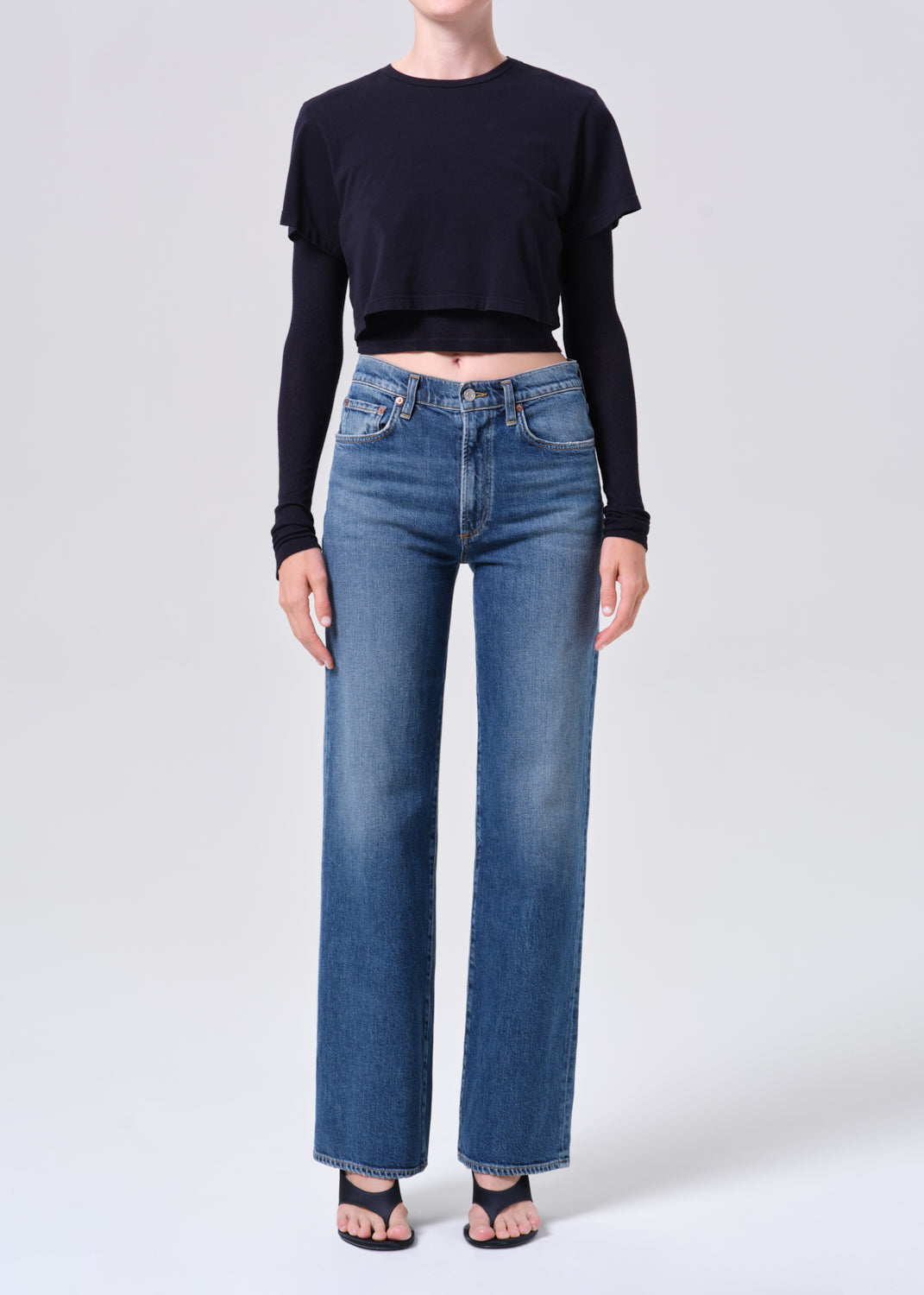 Person wearing blue jeans and a black crop top on a white background