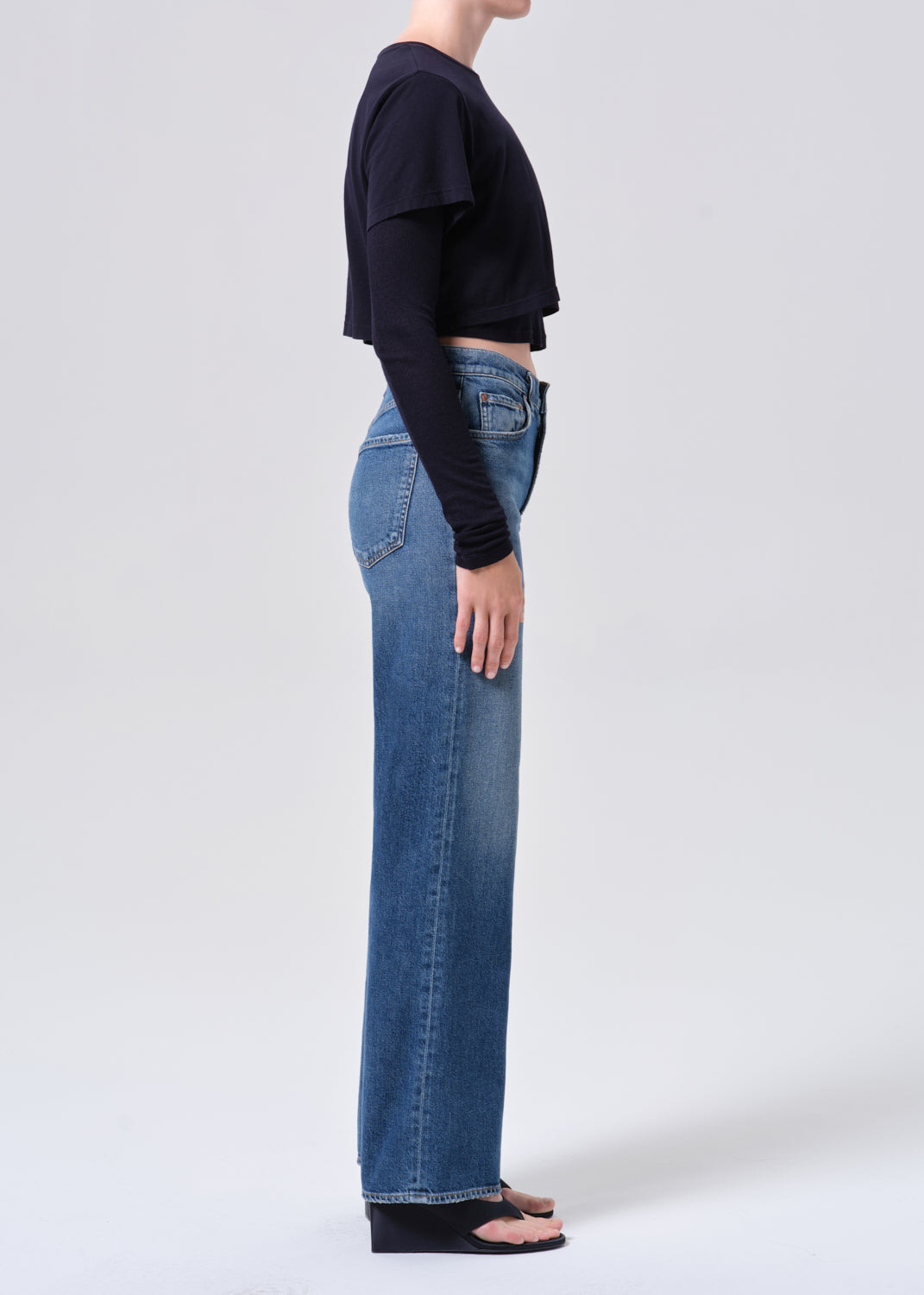 Person wearing blue jeans and a black top on a white background