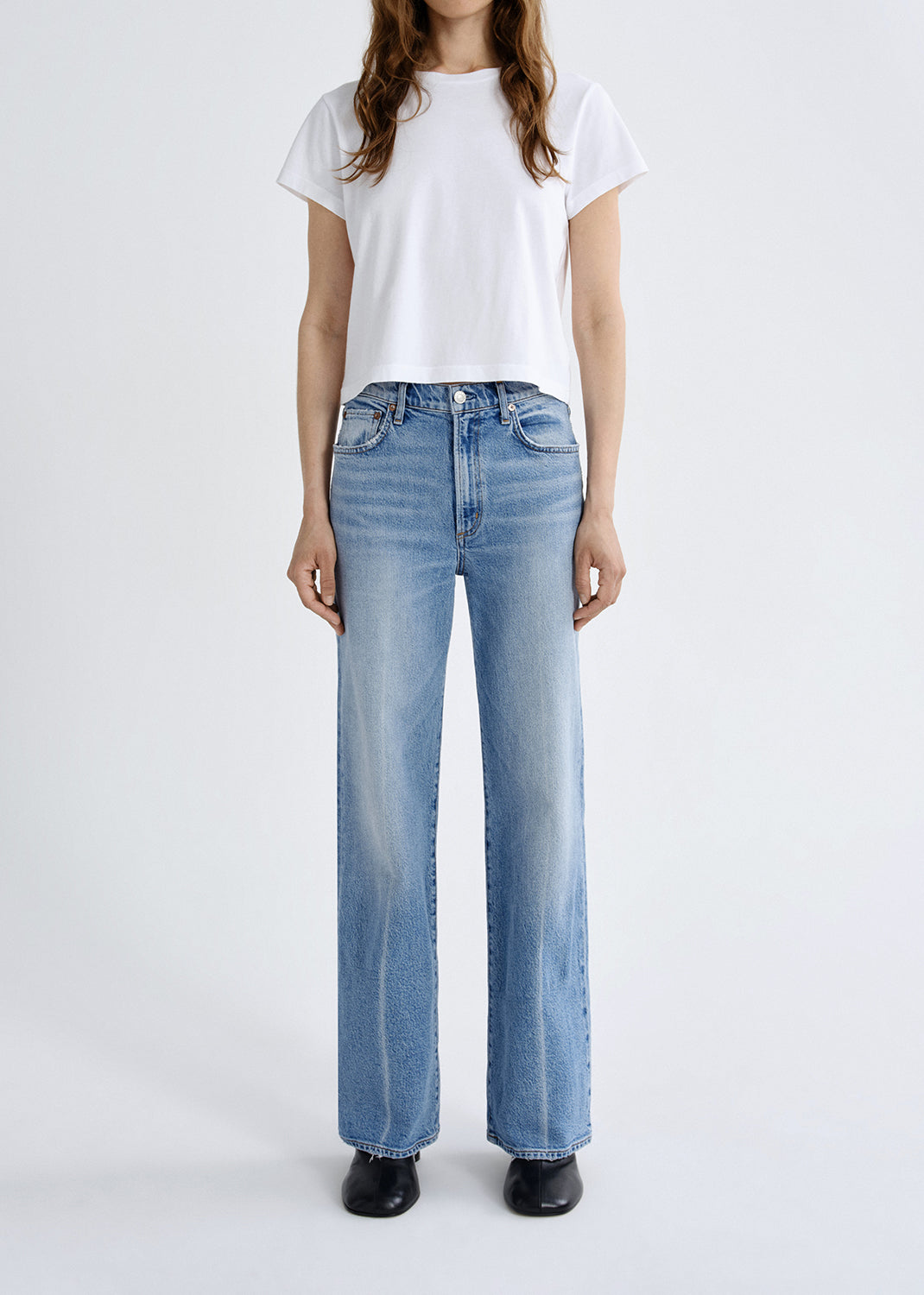 Person wearing light blue jeans and a white t-shirt on a white background