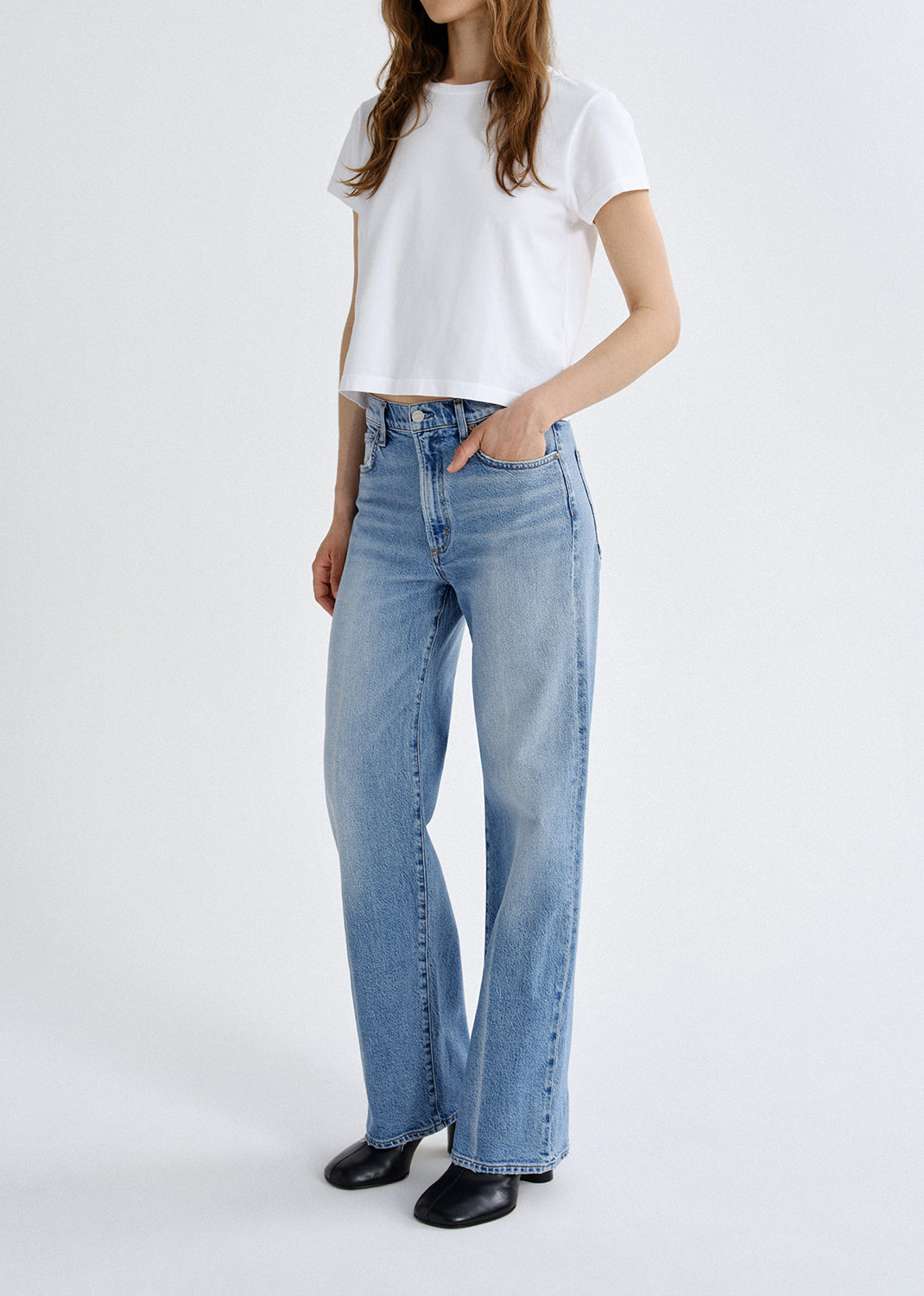 Person wearing light blue jeans and a white top on a white background