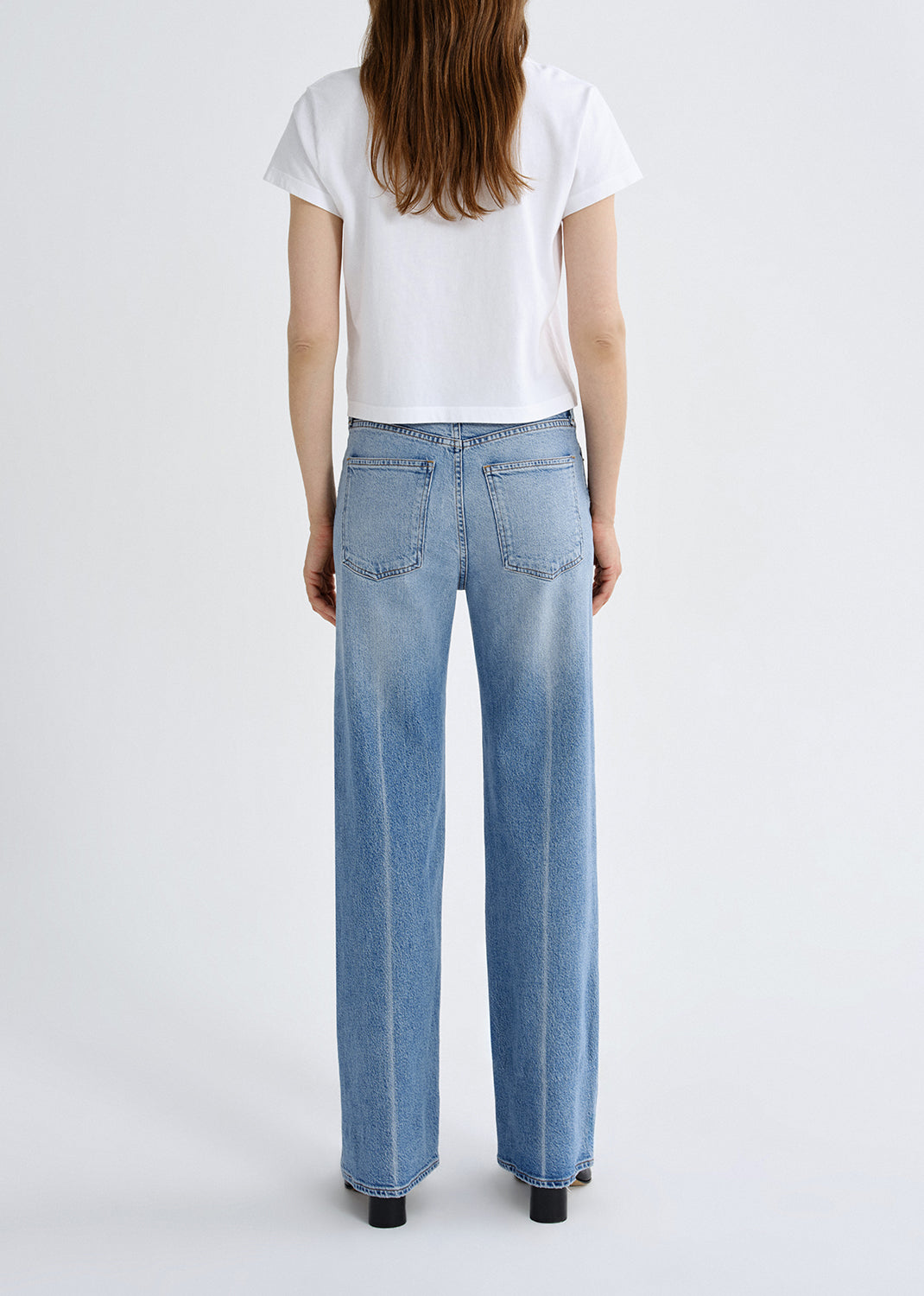 Person wearing light blue jeans and a white t-shirt on a plain background
